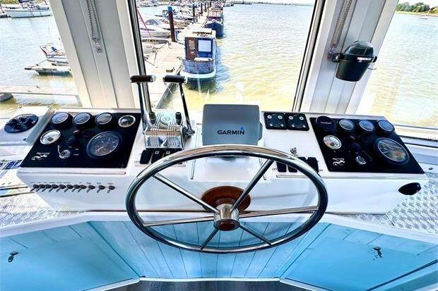 Steering wheel and controls of a 2007 Houseboat Original model overlooking a marina.