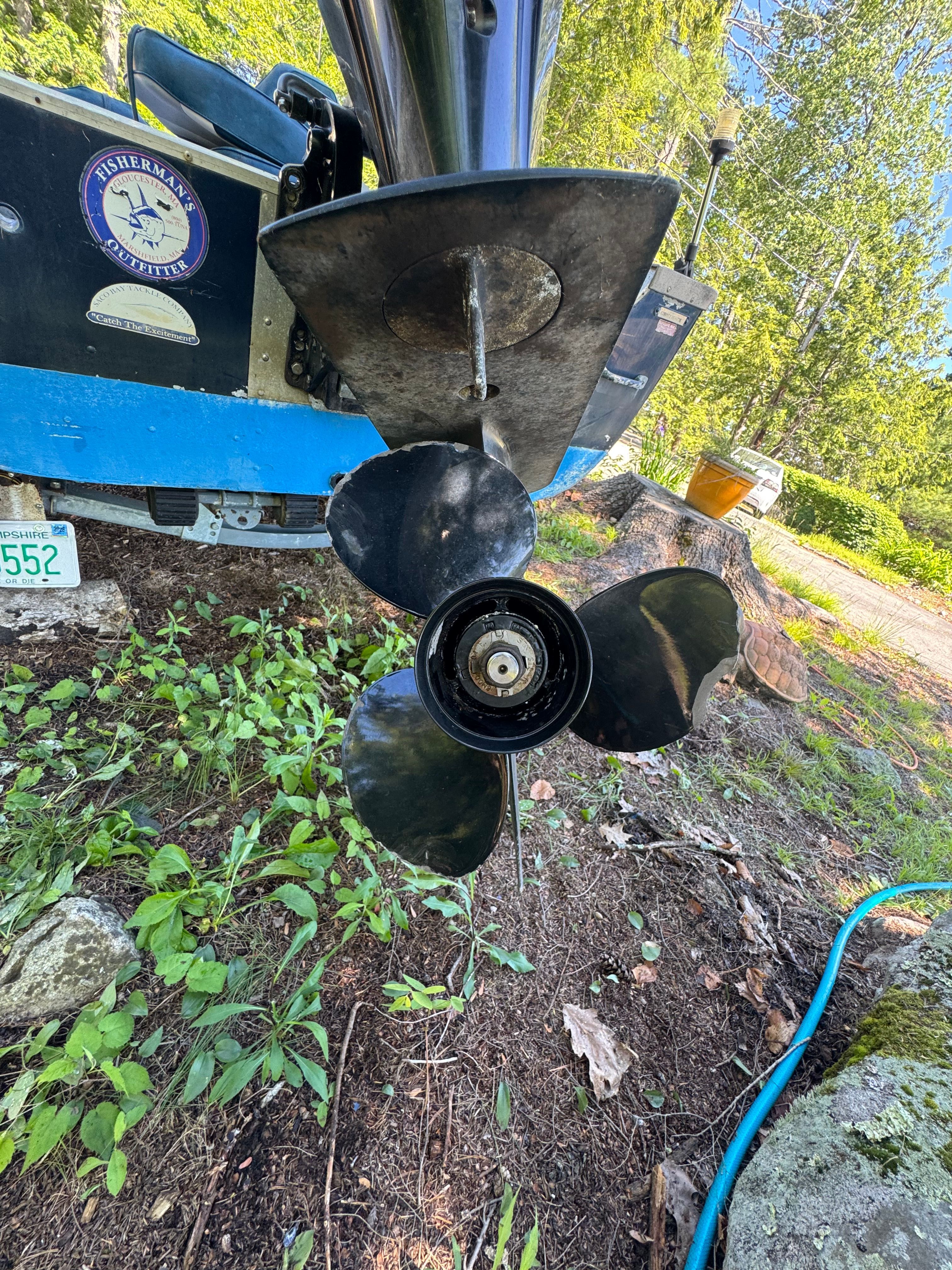 A boat motor with a three-blade propeller on dry land.