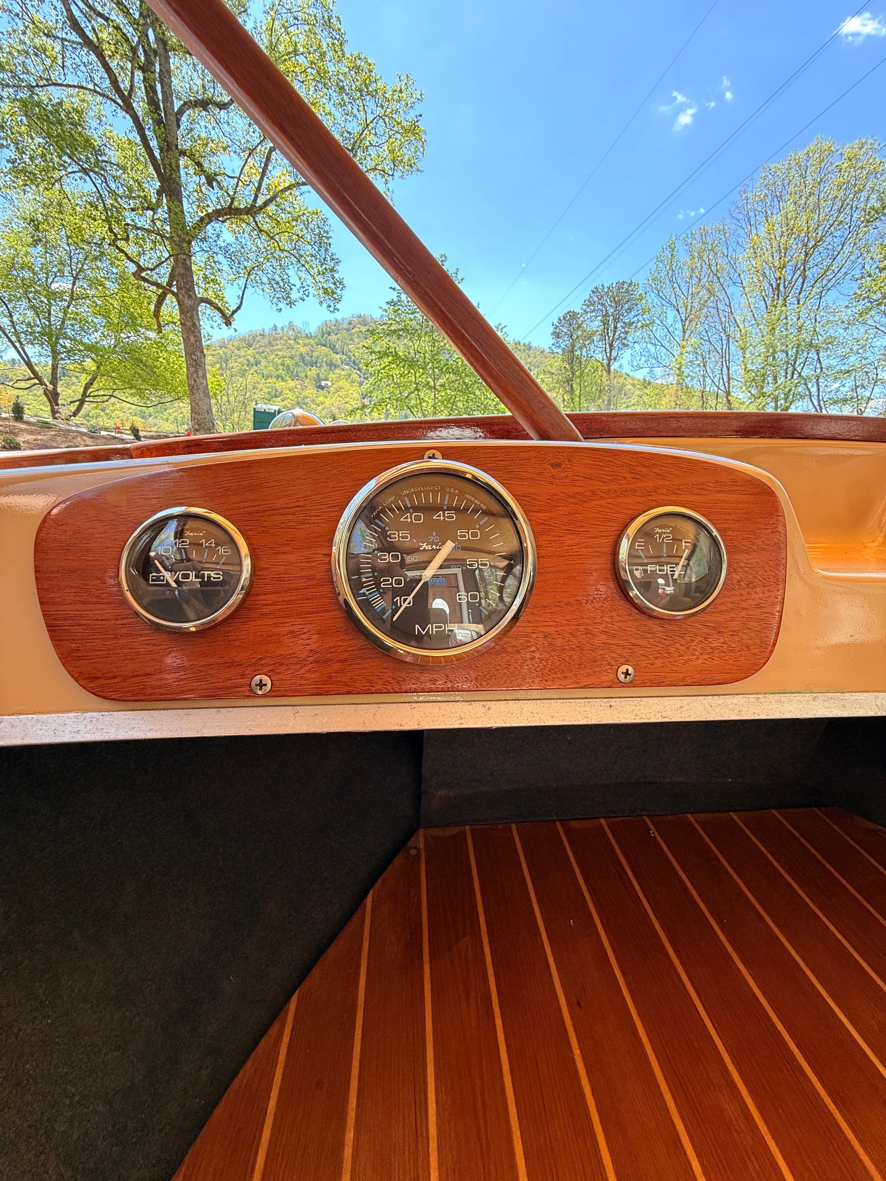 Dashboard of a vintage boat with a speedometer and wooden flooring.