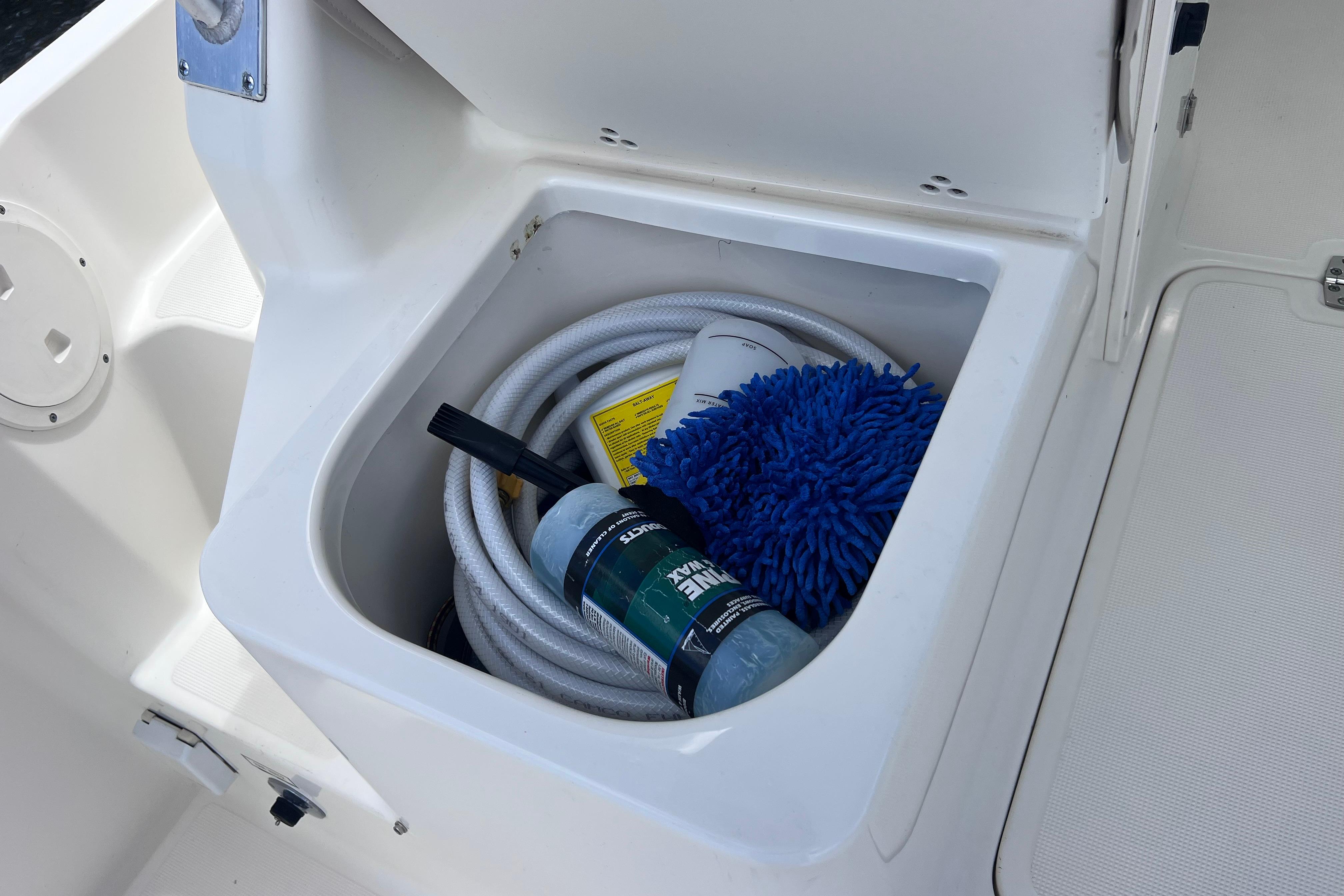 Storage compartment on a 2004 Pursuit 2870 Walkaround boat with cleaning supplies and hose.