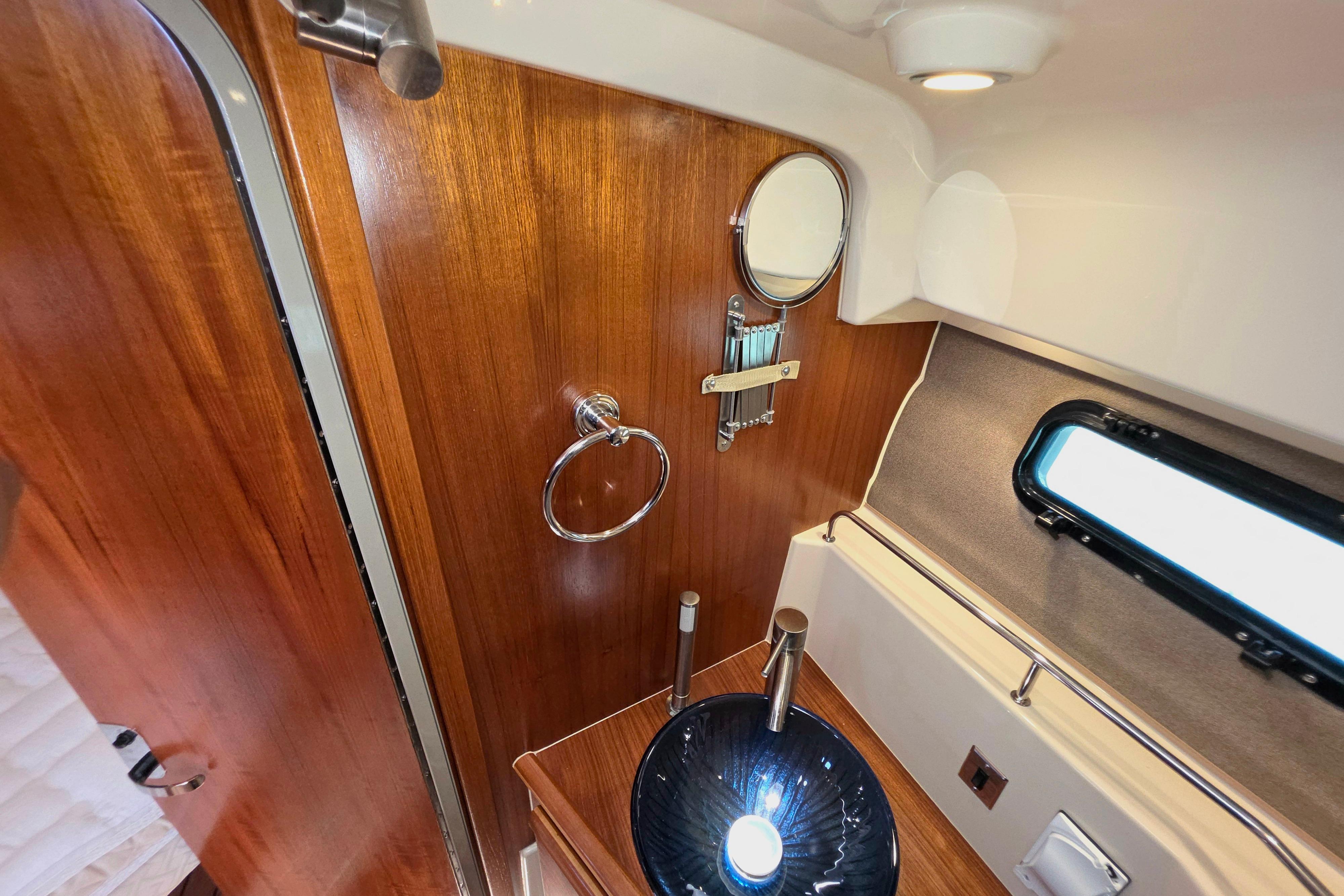 2021 Ranger Tug R27 bathroom with wood paneling, round mirror, and modern sink.