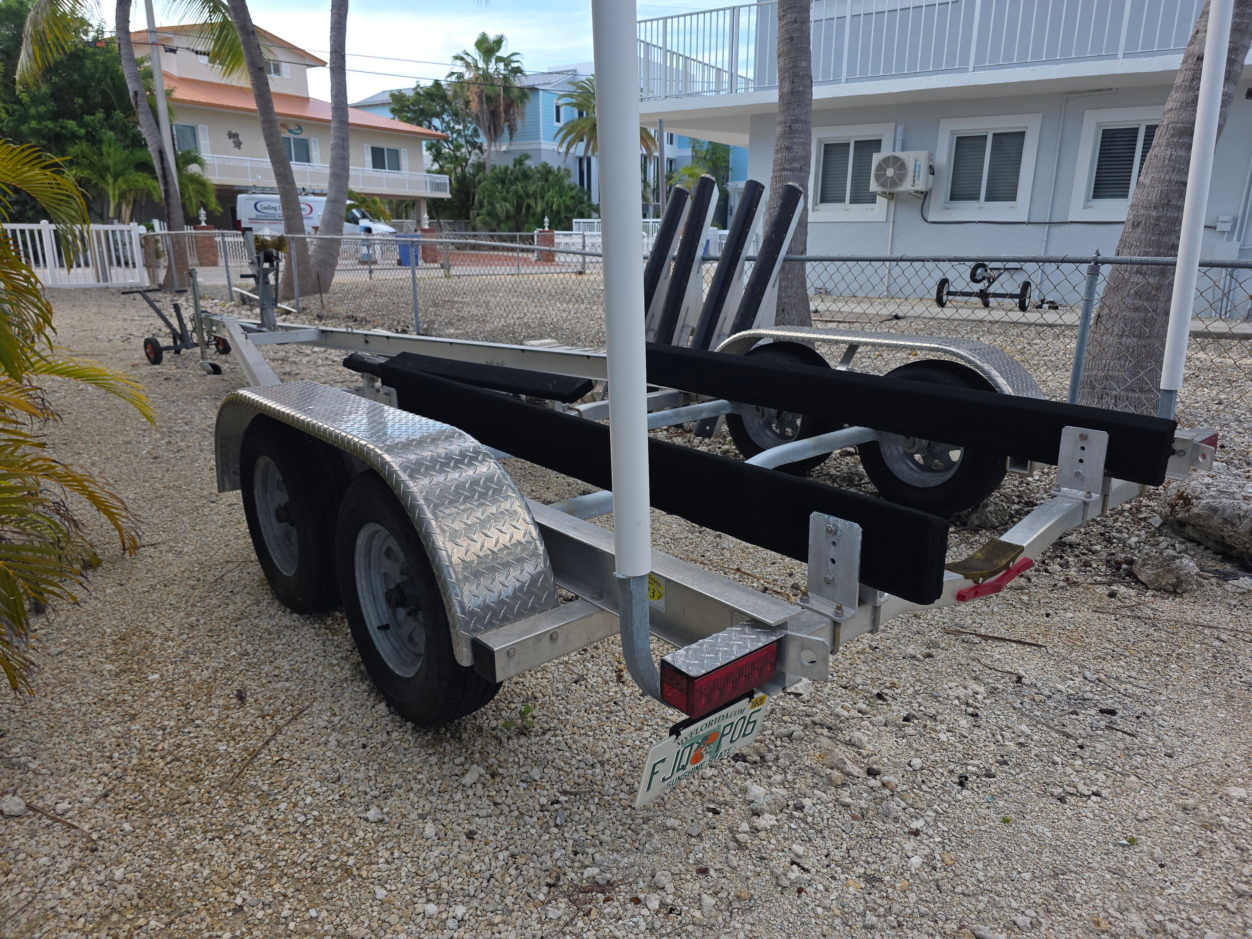 Boat trailer on gravel path in front of houses and palm trees.