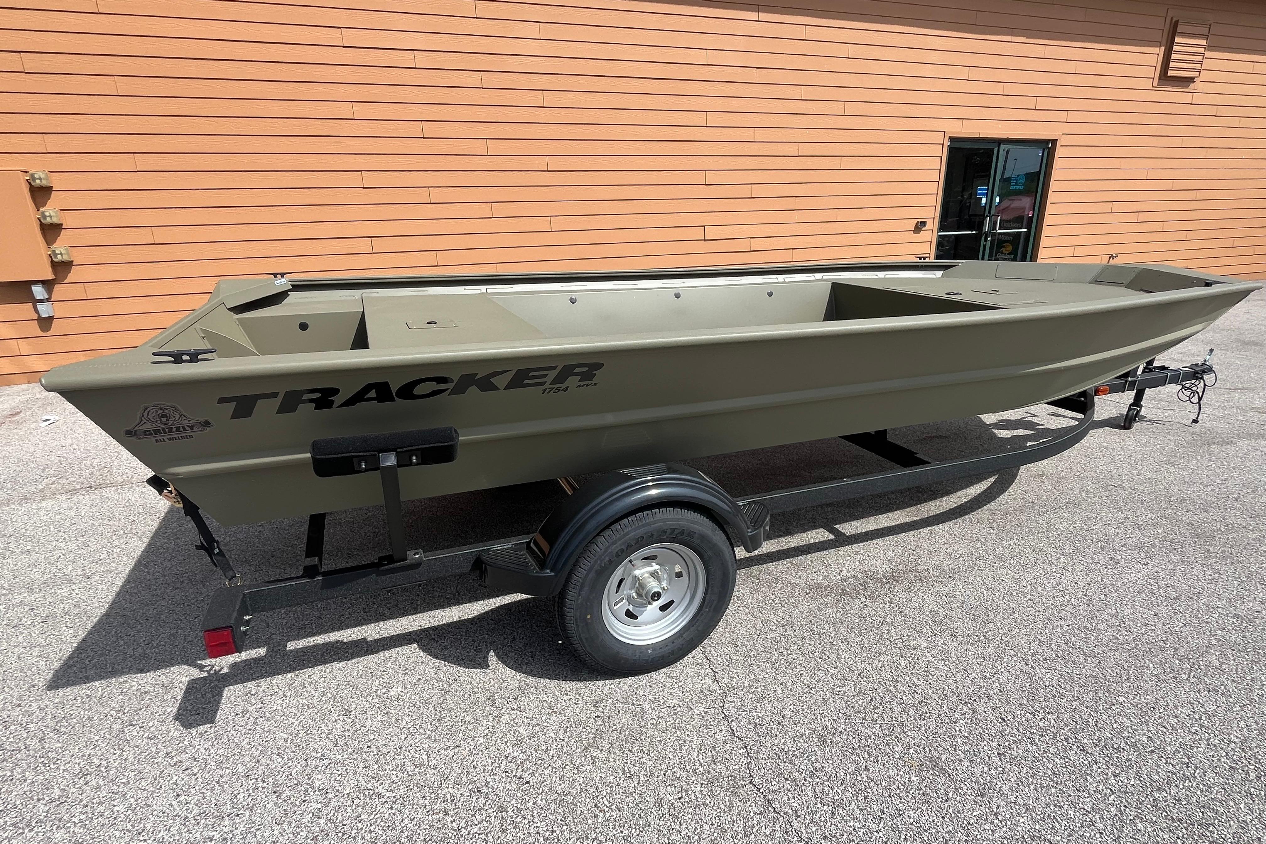 2026 Tracker Grizzly 1754 Utility boat on trailer, parked outside an orange building.