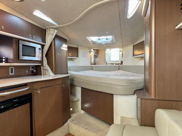 2014 Sea Ray 330 Sundancer cabin interior with bed, kitchenette, and wood cabinetry.