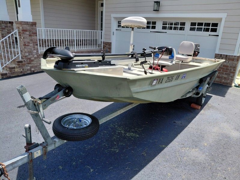 A 1999 SeaArk jon boat is on a trailer in front of a garage.