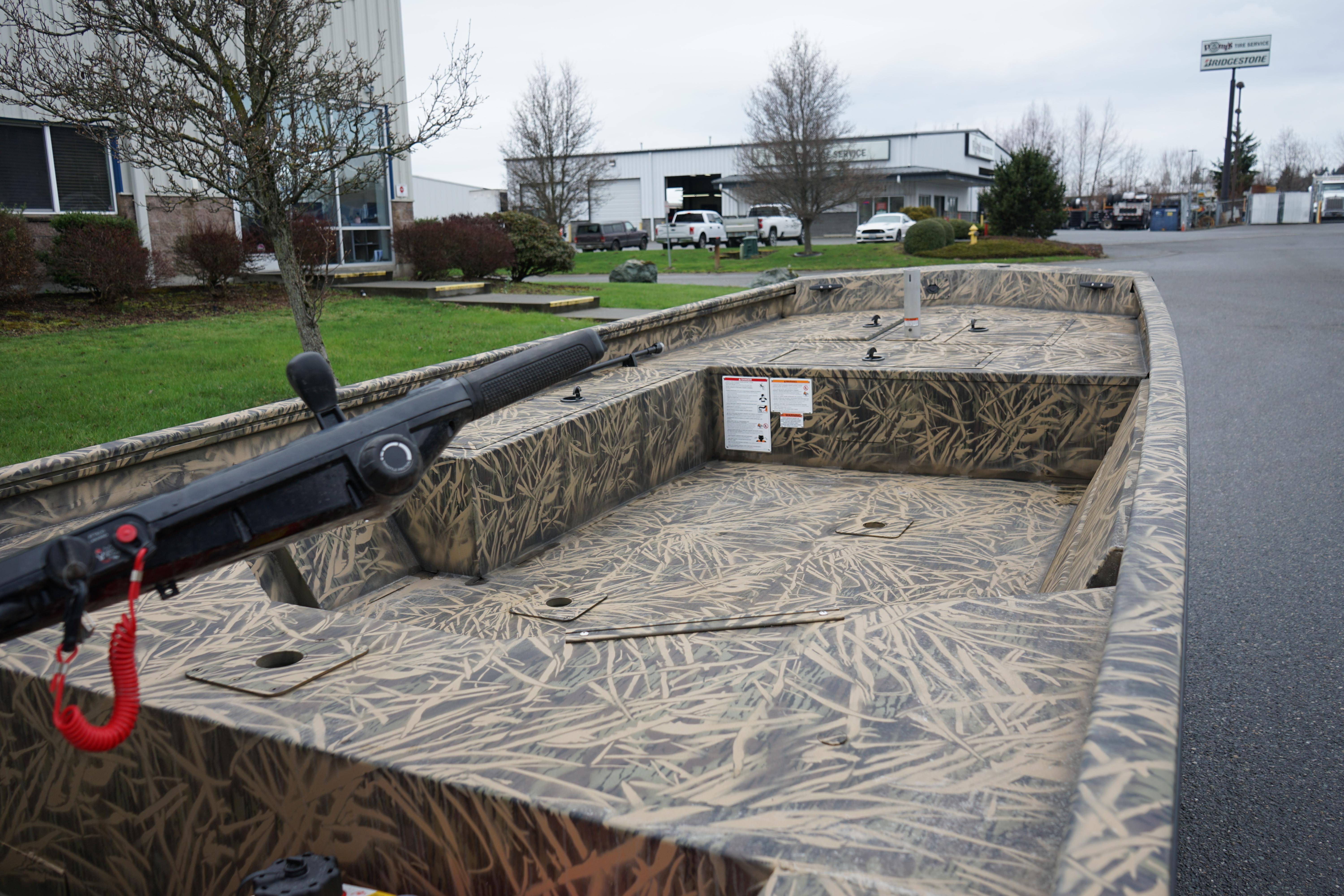 2024 Lund 1760 Predator Tiller boat with camouflage design, parked outdoors.