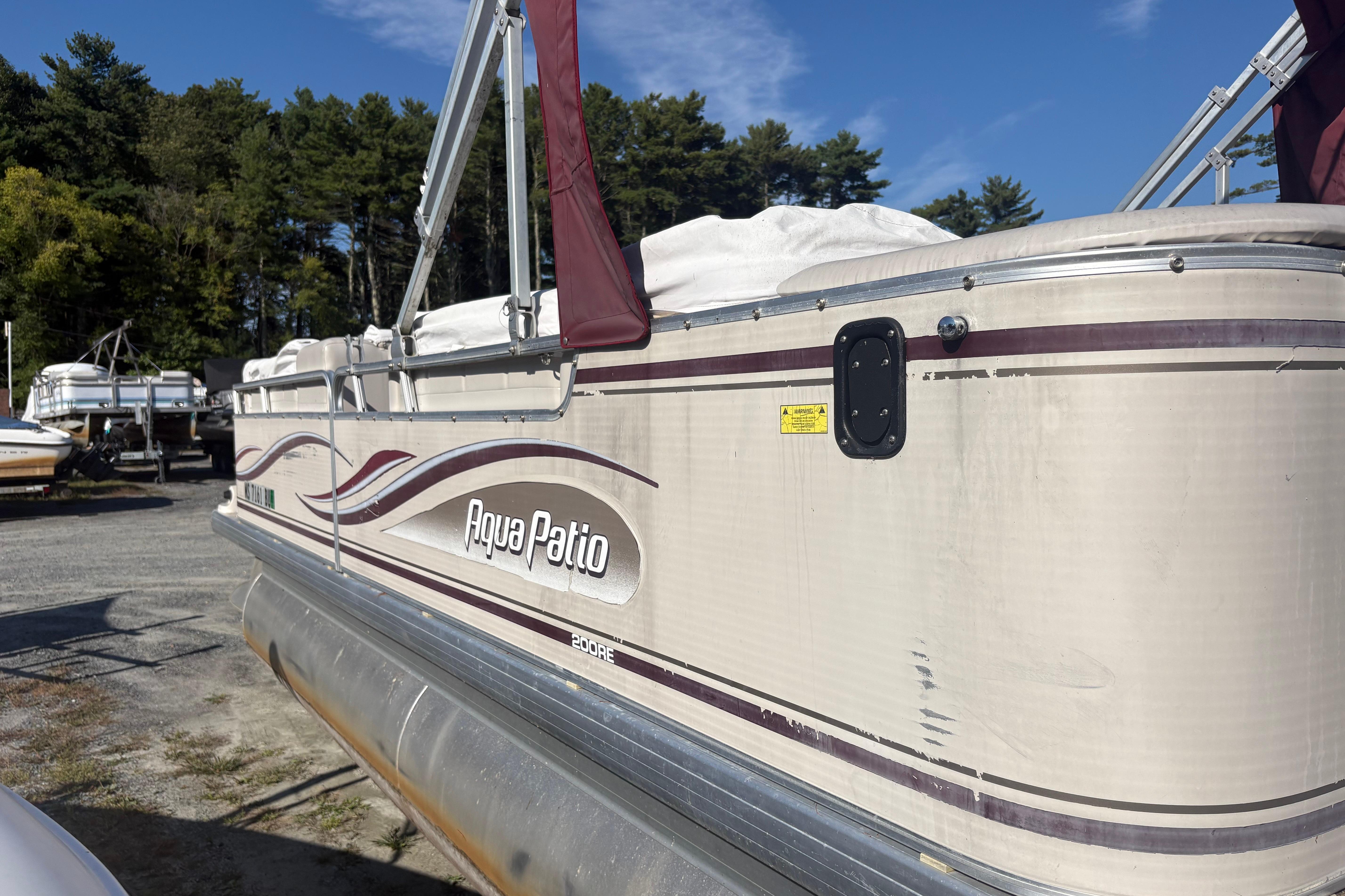 2003 Aqua Patio 200RE pontoon boat in storage, surrounded by trees and other boats.