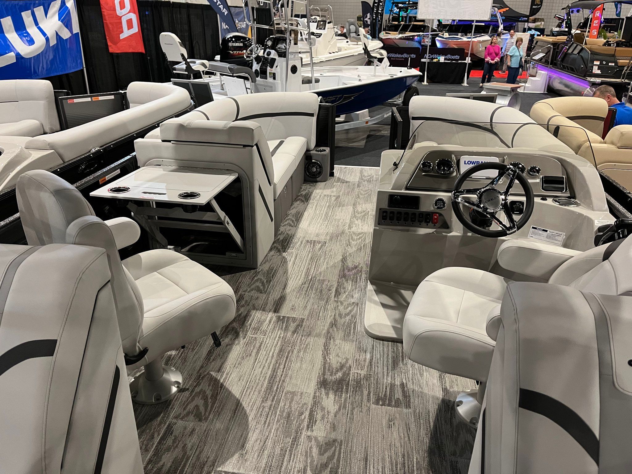 Interior of a modern pontoon boat with gray and white seating, table, and helm console.