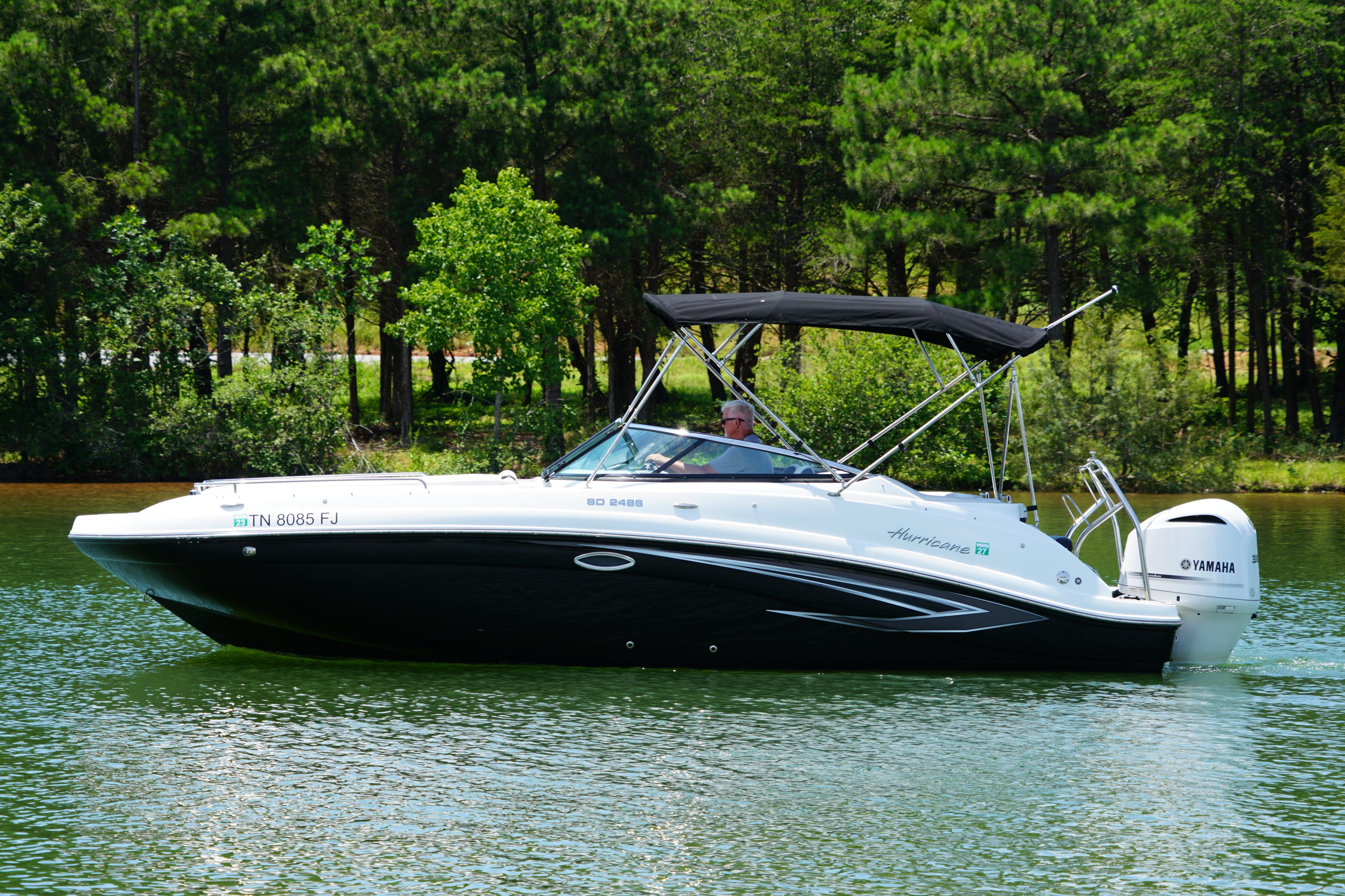 2020 Hurricane SunDeck 2486 OB boat cruising on a serene lake with lush green trees.