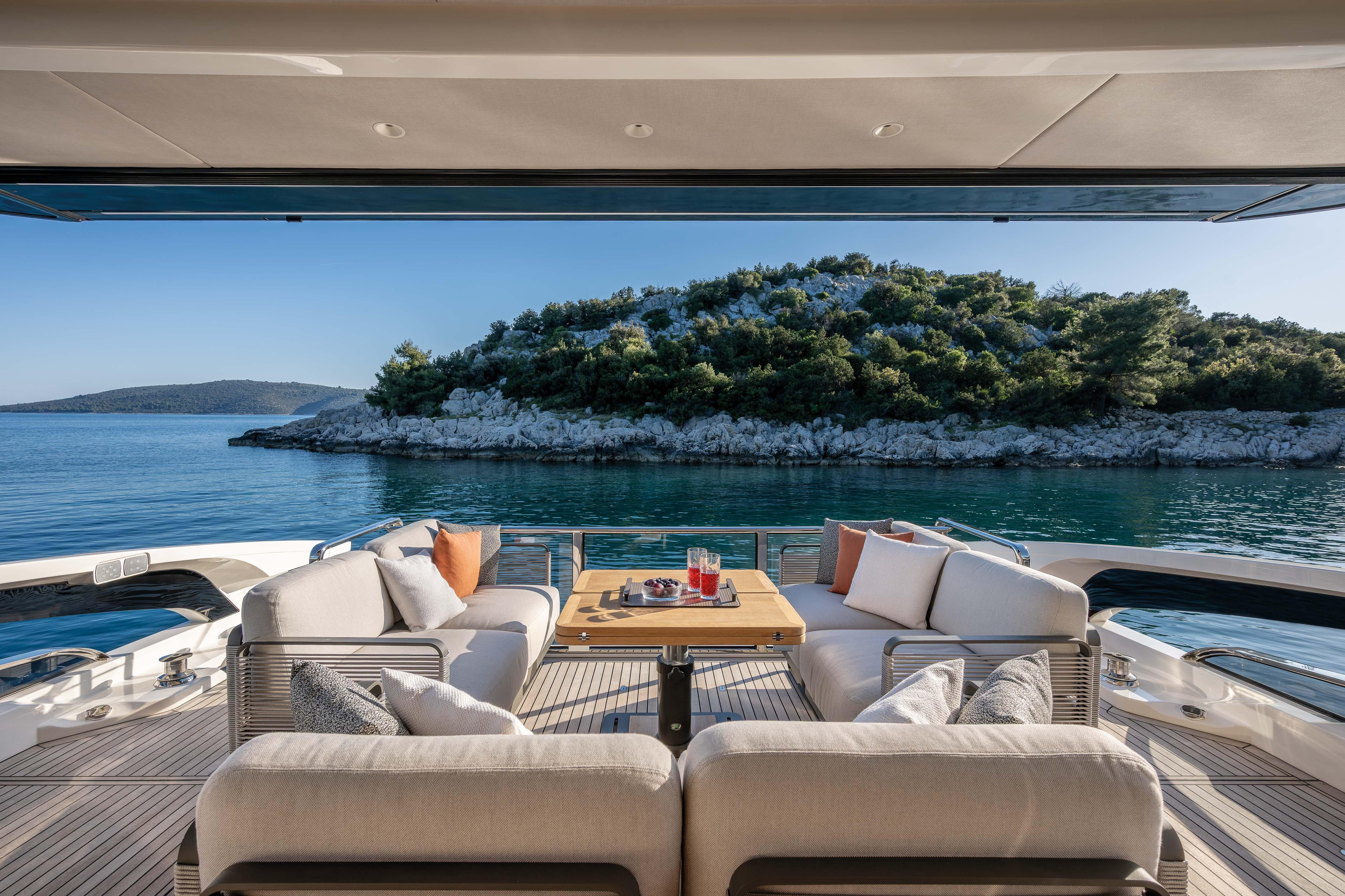 Luxurious yacht with stylish sofas and table, set against a wooded island on calm waters.