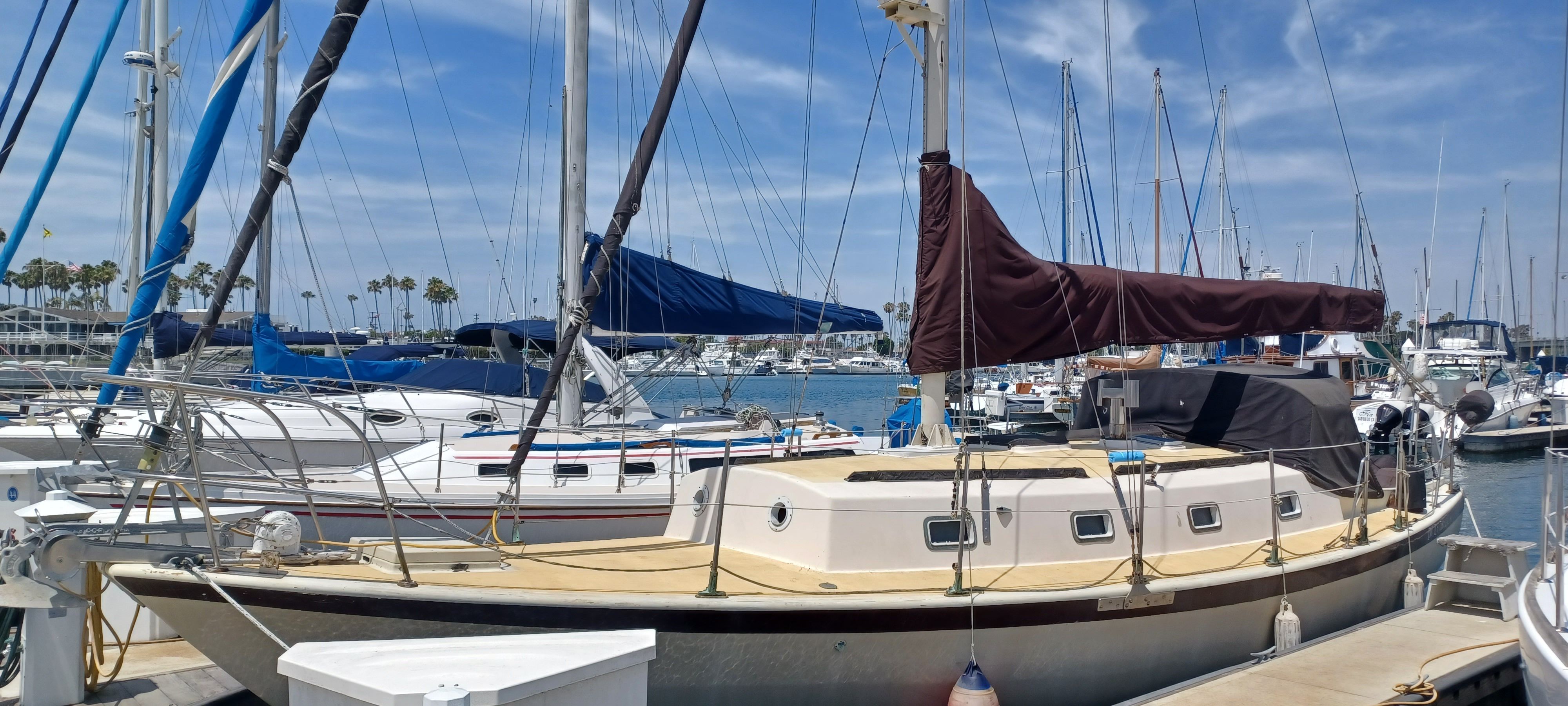 A sailboat docked in a marina, surrounded by other boats, with a brown sail cover.