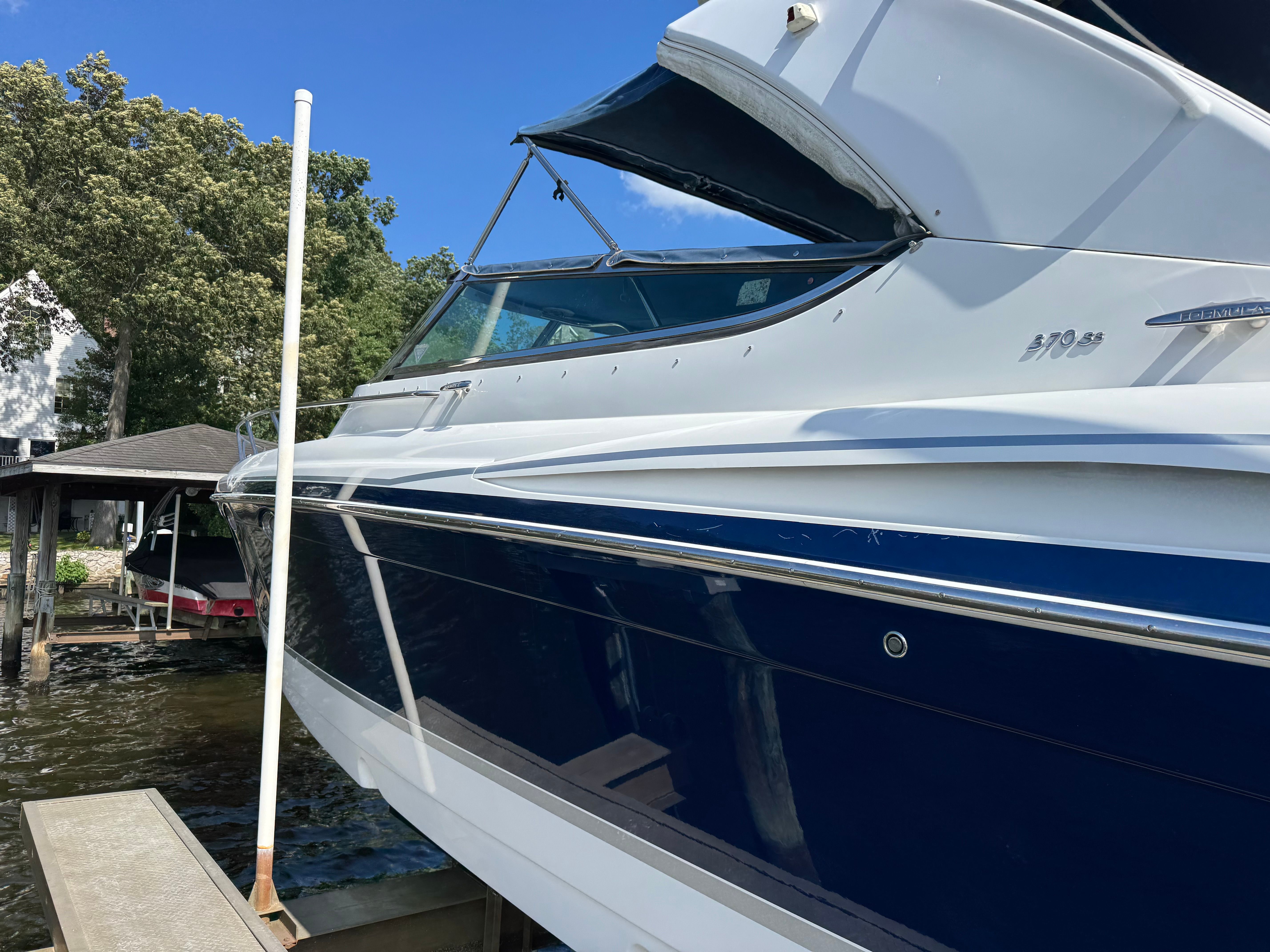 A blue and white boat docked, surrounded by trees and clear sky.