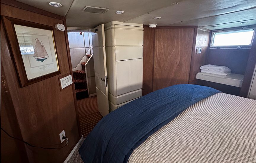 Interior of a yacht with wood-paneled walls, a bed, and a small window.