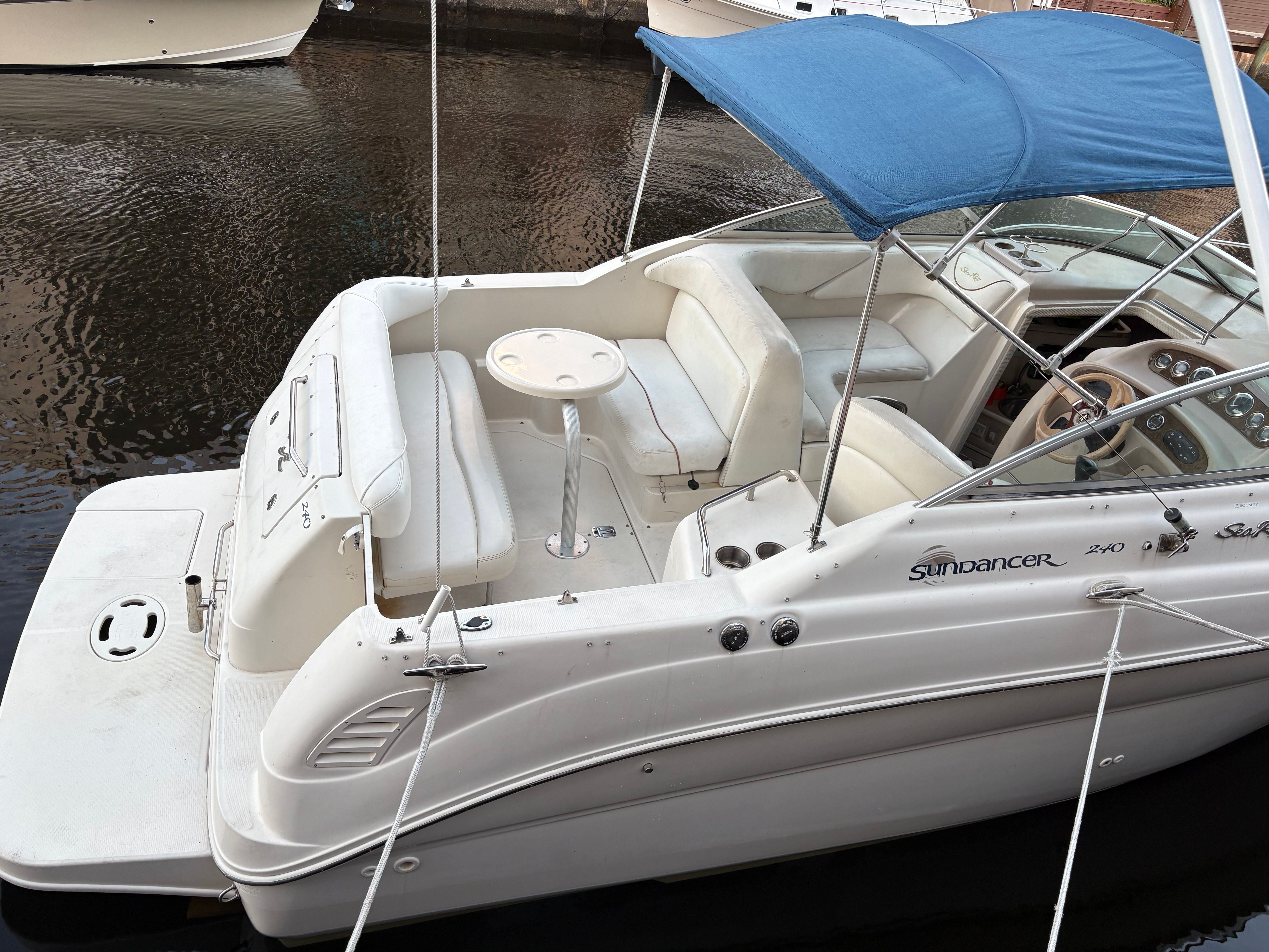 A 2001 Sea Ray 240 Sundancer with a blue sunshade, docked at a pier.