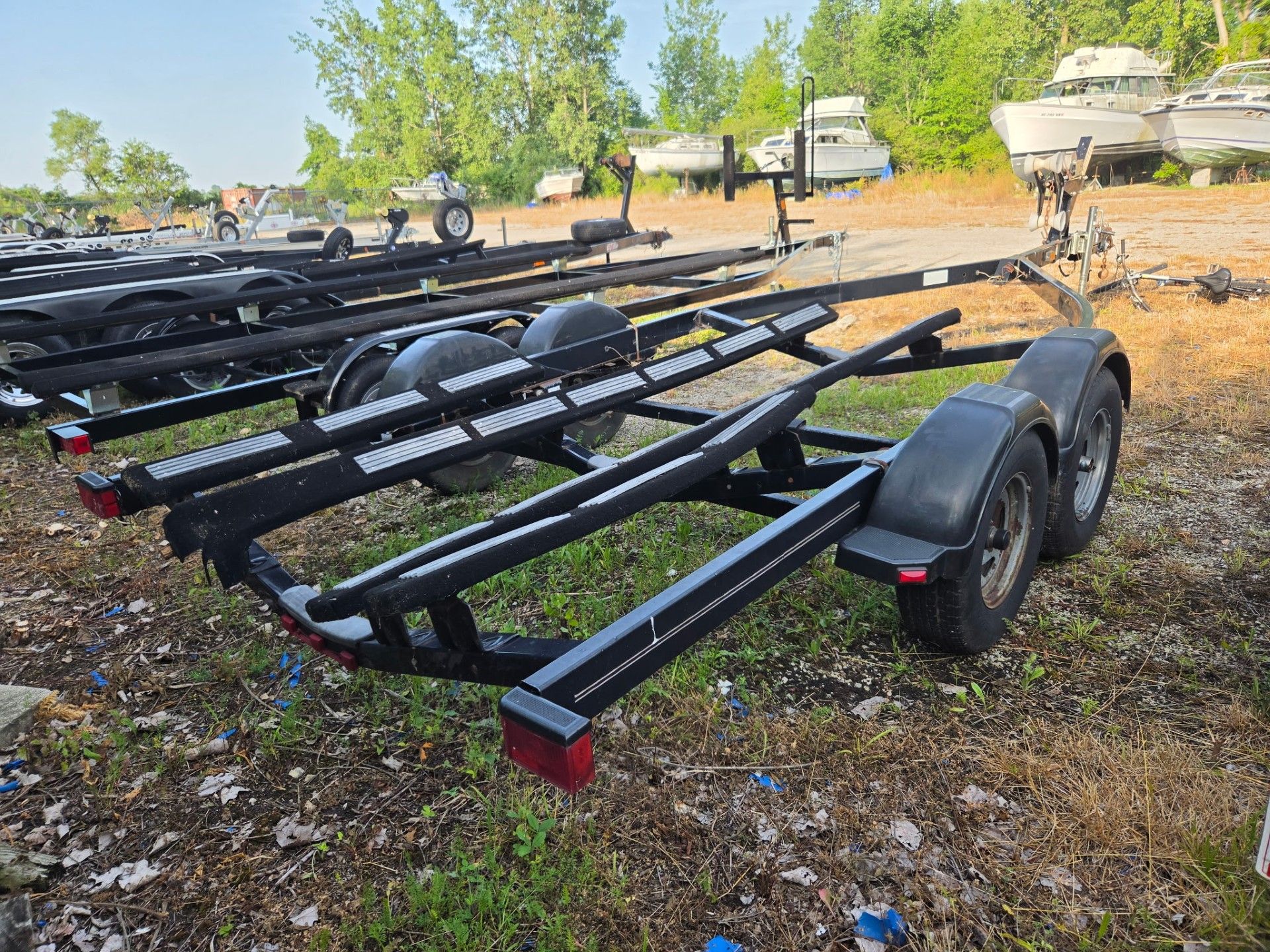 A boat trailer sits on grassy terrain with several boats in the background.