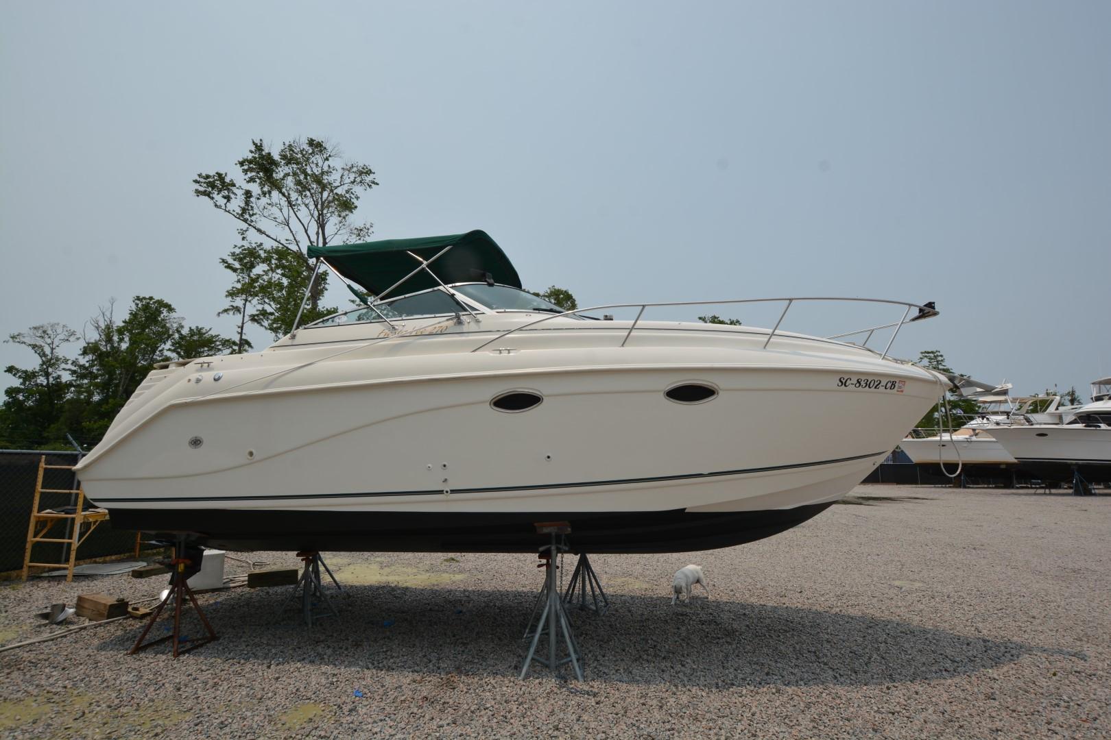 1999 Rinker 270 Fiesta Vee boat on stands, with green canopy, in a gravel lot.