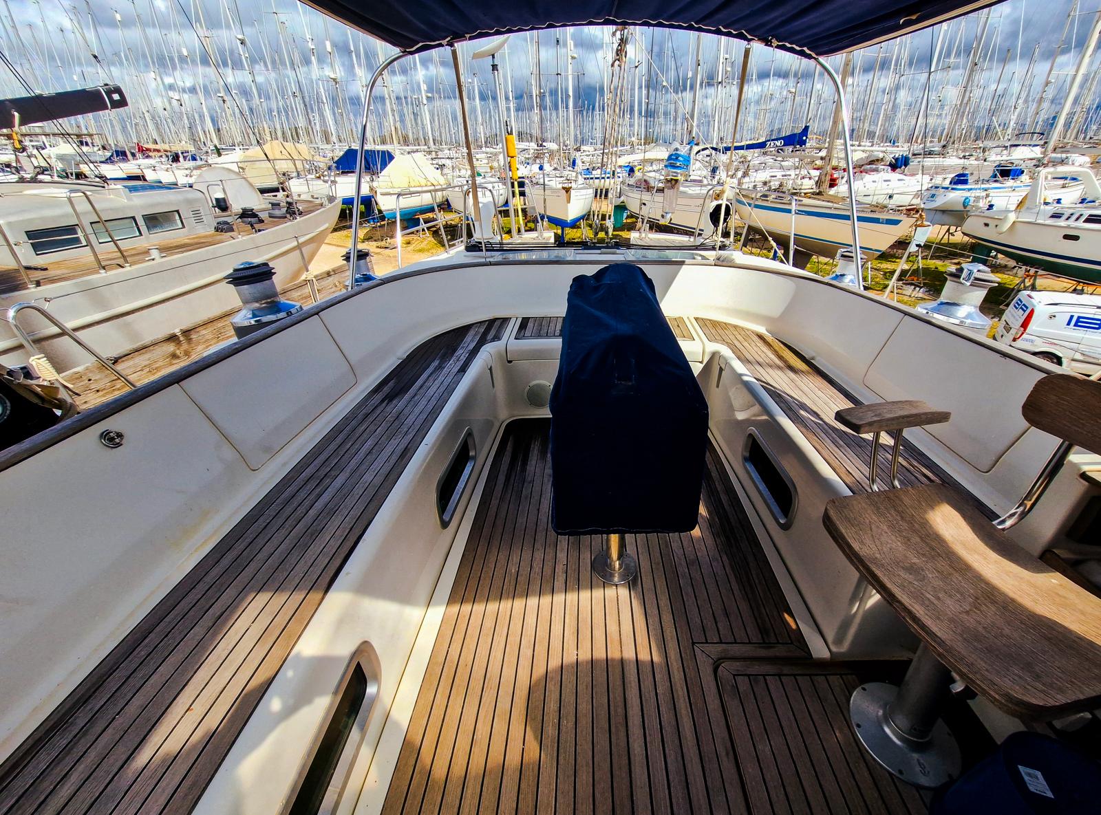 2004 Beneteau 57 yacht cockpit with wooden deck, marina view, and covered helm.
