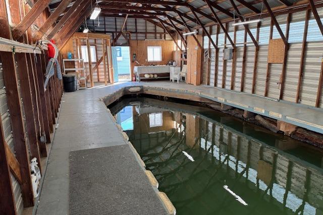1960 custom boathouse interior with wooden beams, dock, and water channel.