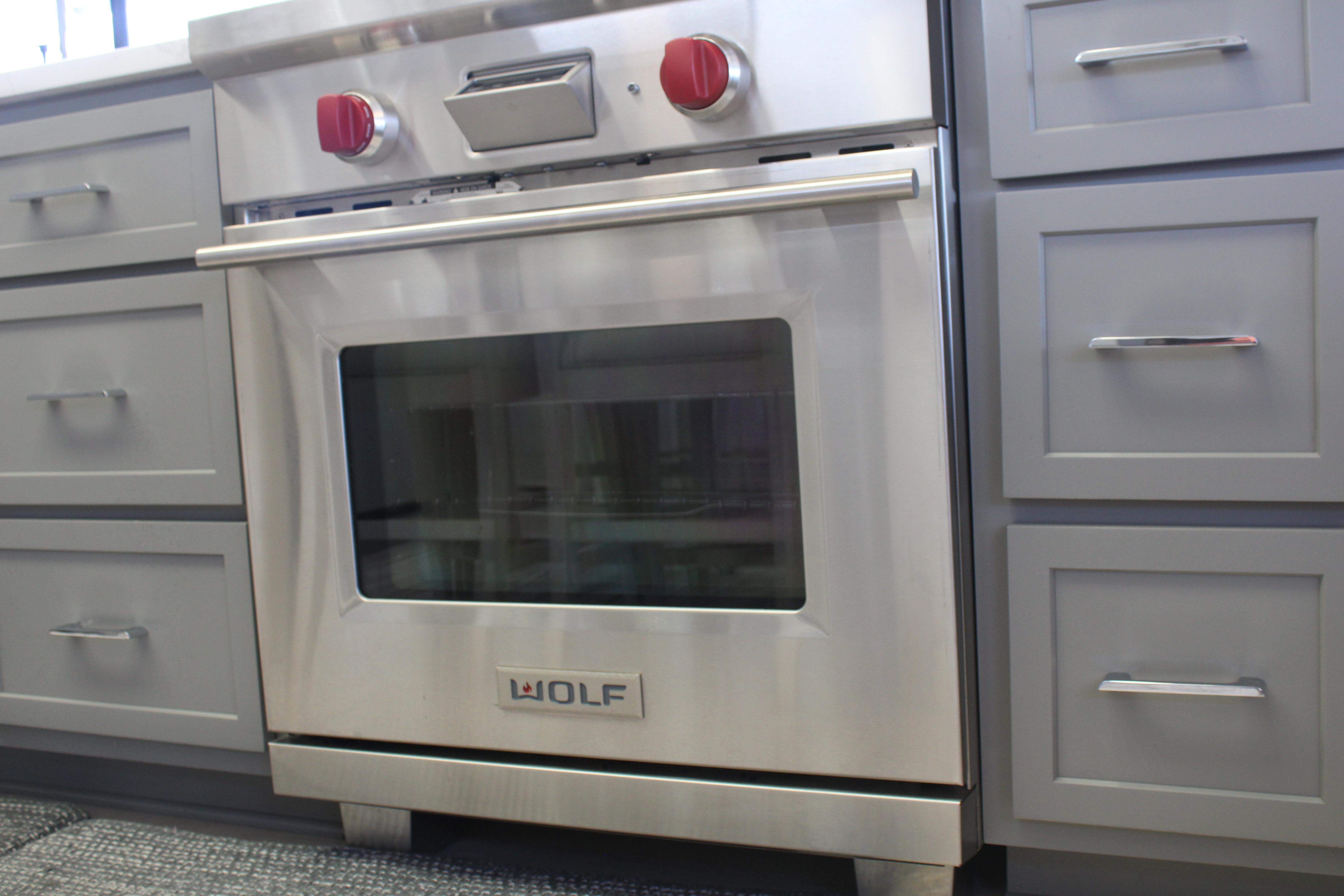 Stainless steel Wolf oven with red knobs, surrounded by gray cabinetry.