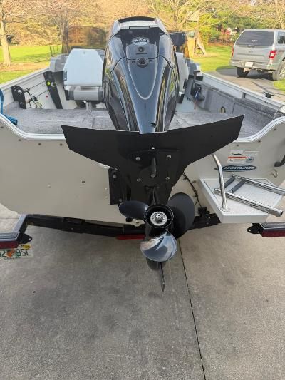 A boat with an outboard motor is on a trailer in a driveway.