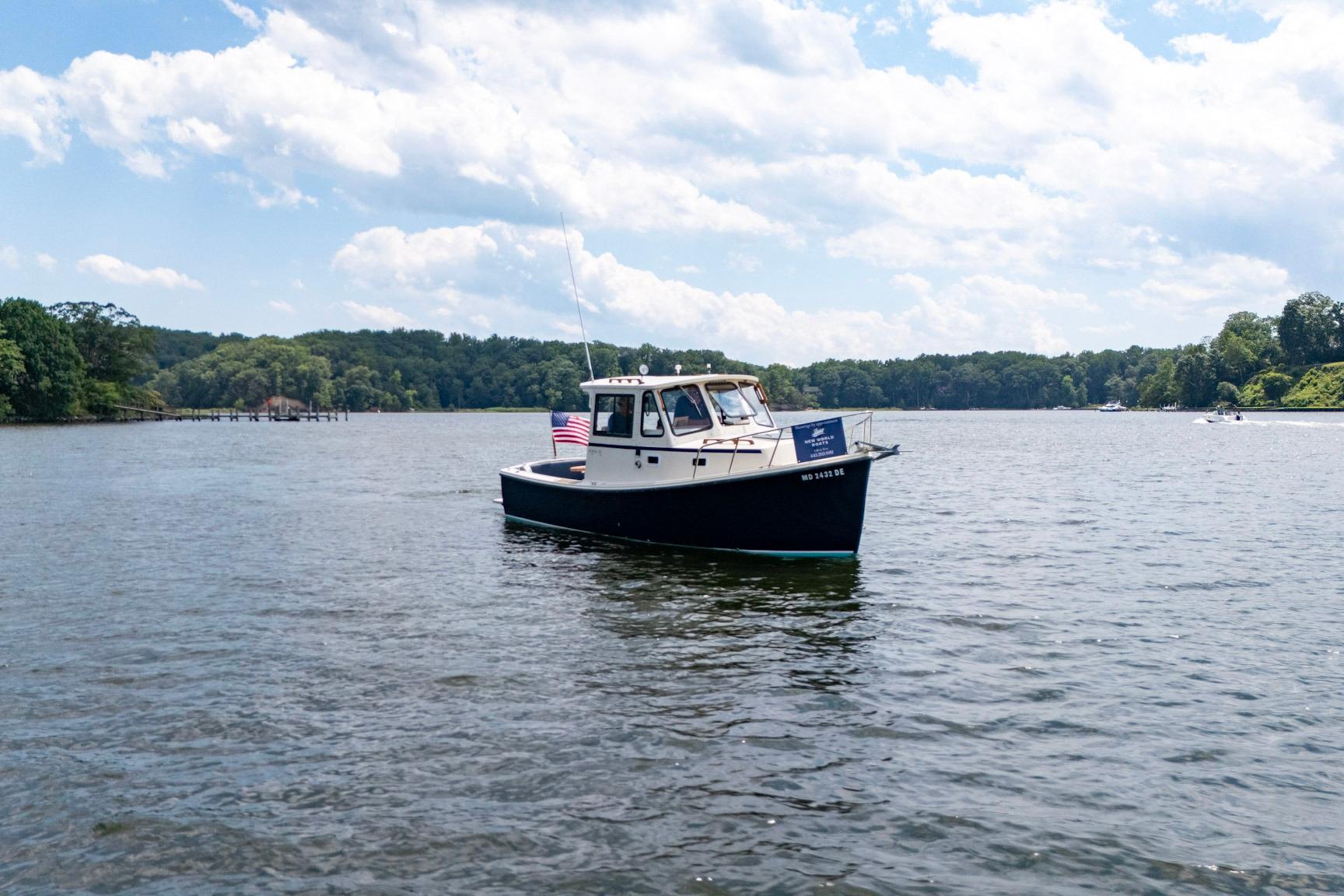 2006 Atlas Boat Works Acadia 25 on a serene lake with lush green shoreline.