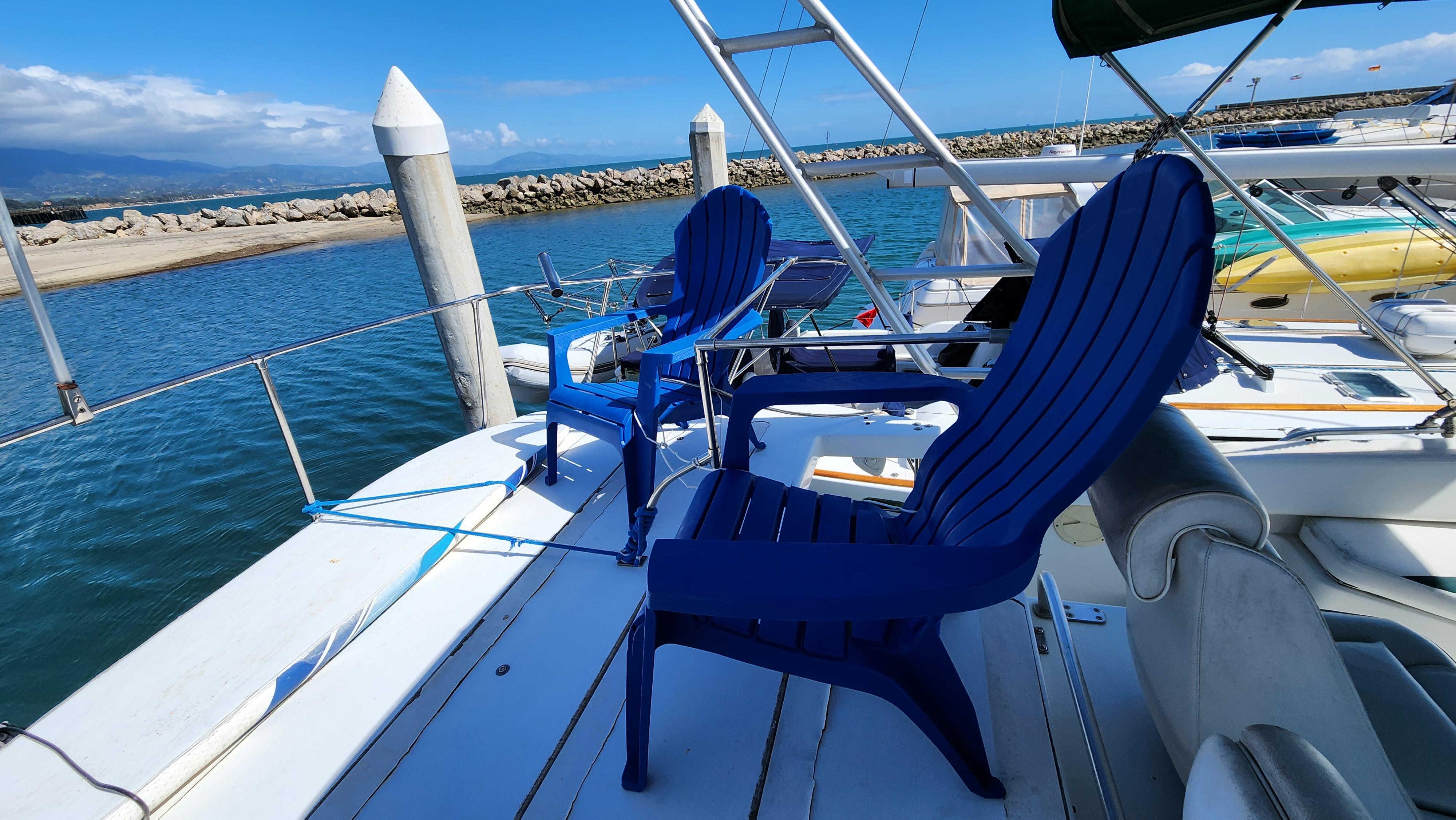1995 Mainship 40 Sedan Bridge with blue chairs on deck, docked by a scenic waterfront.