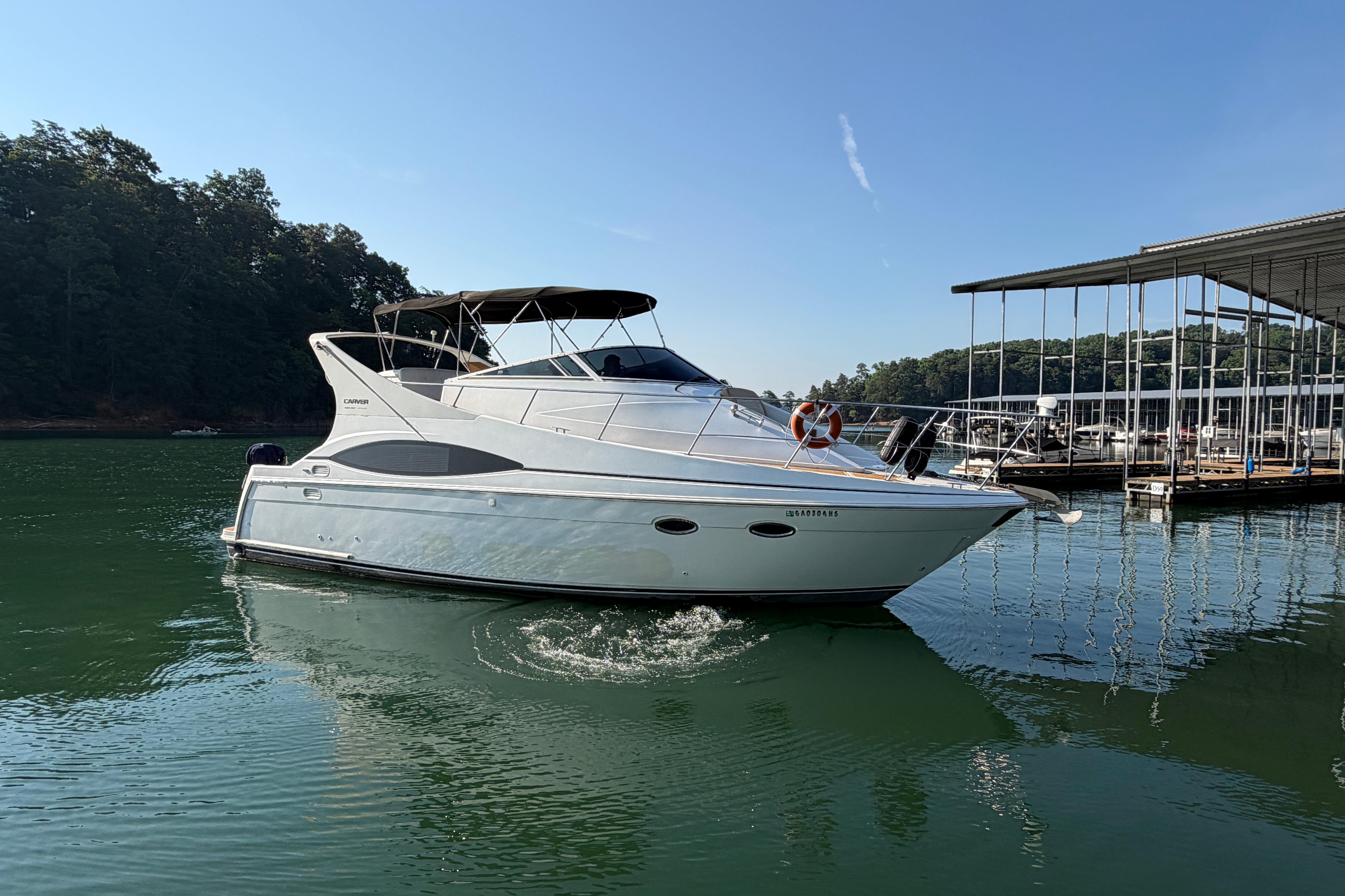 2003 Carver 350 Mariner yacht on calm water near a marina, under clear blue sky.