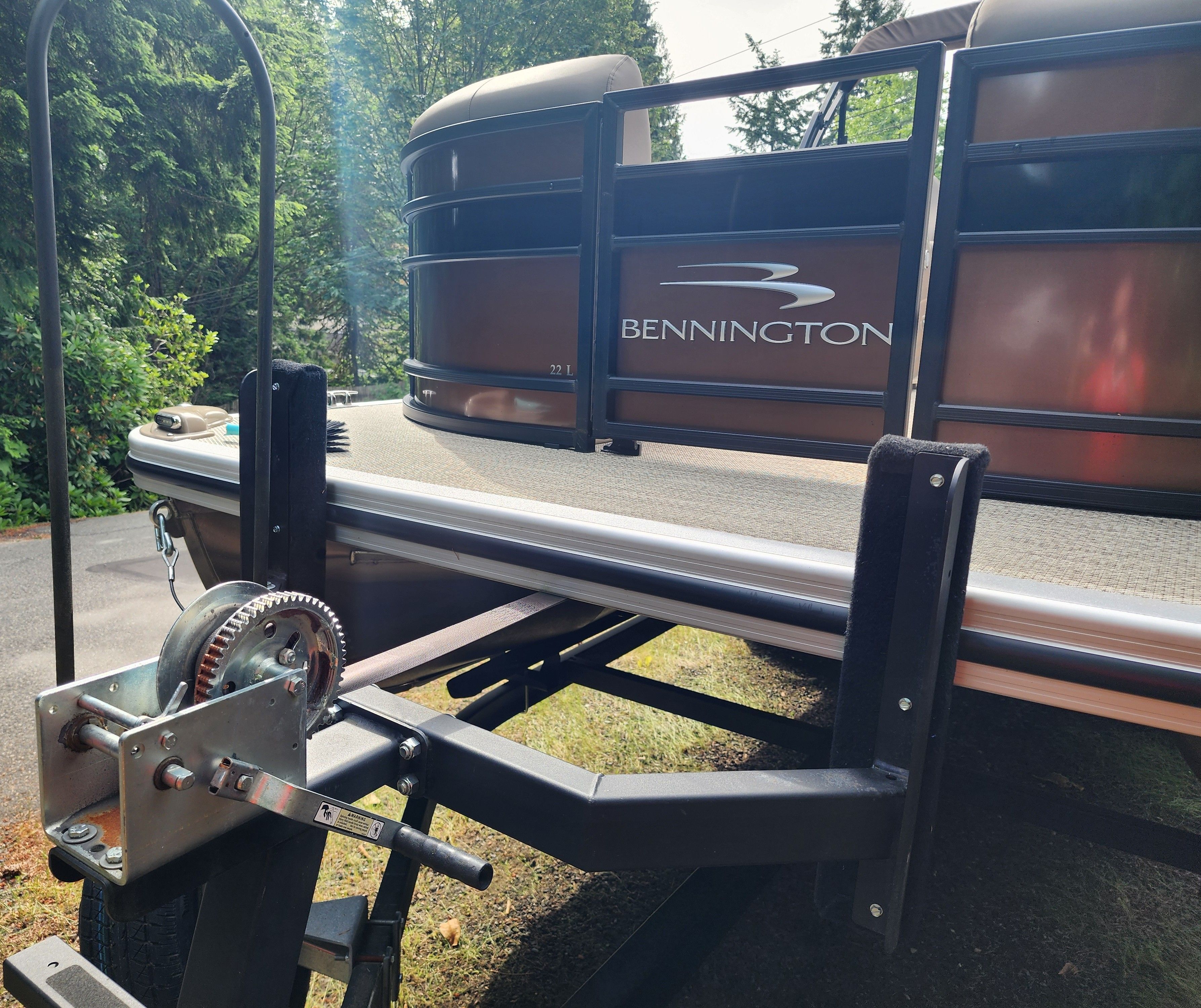 A Bennington 22 LSB pontoon boat on a trailer, surrounded by trees.