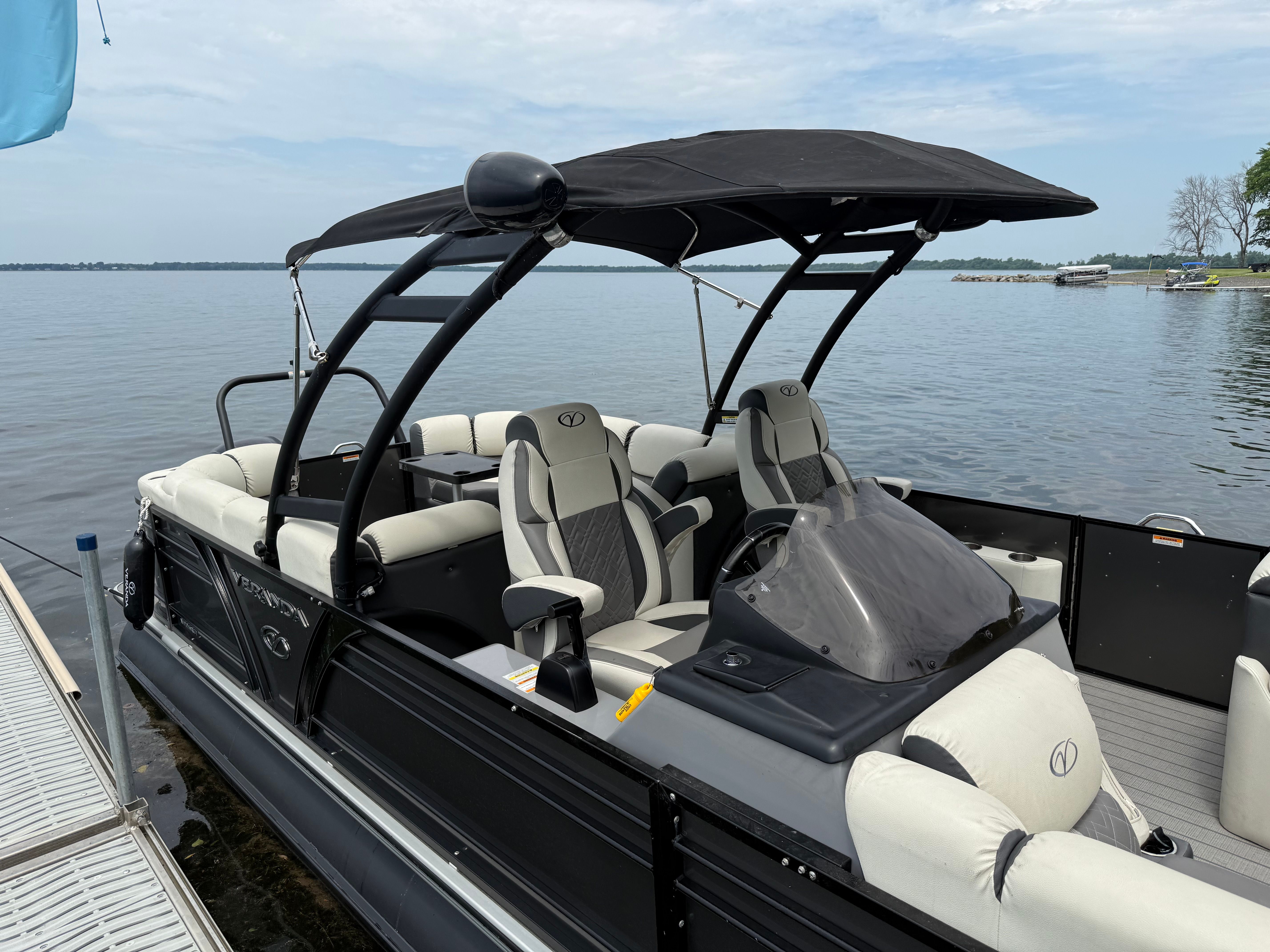 A 2024 Veranda VP 25RCT pontoon boat with a black canopy and gray seats by the water.