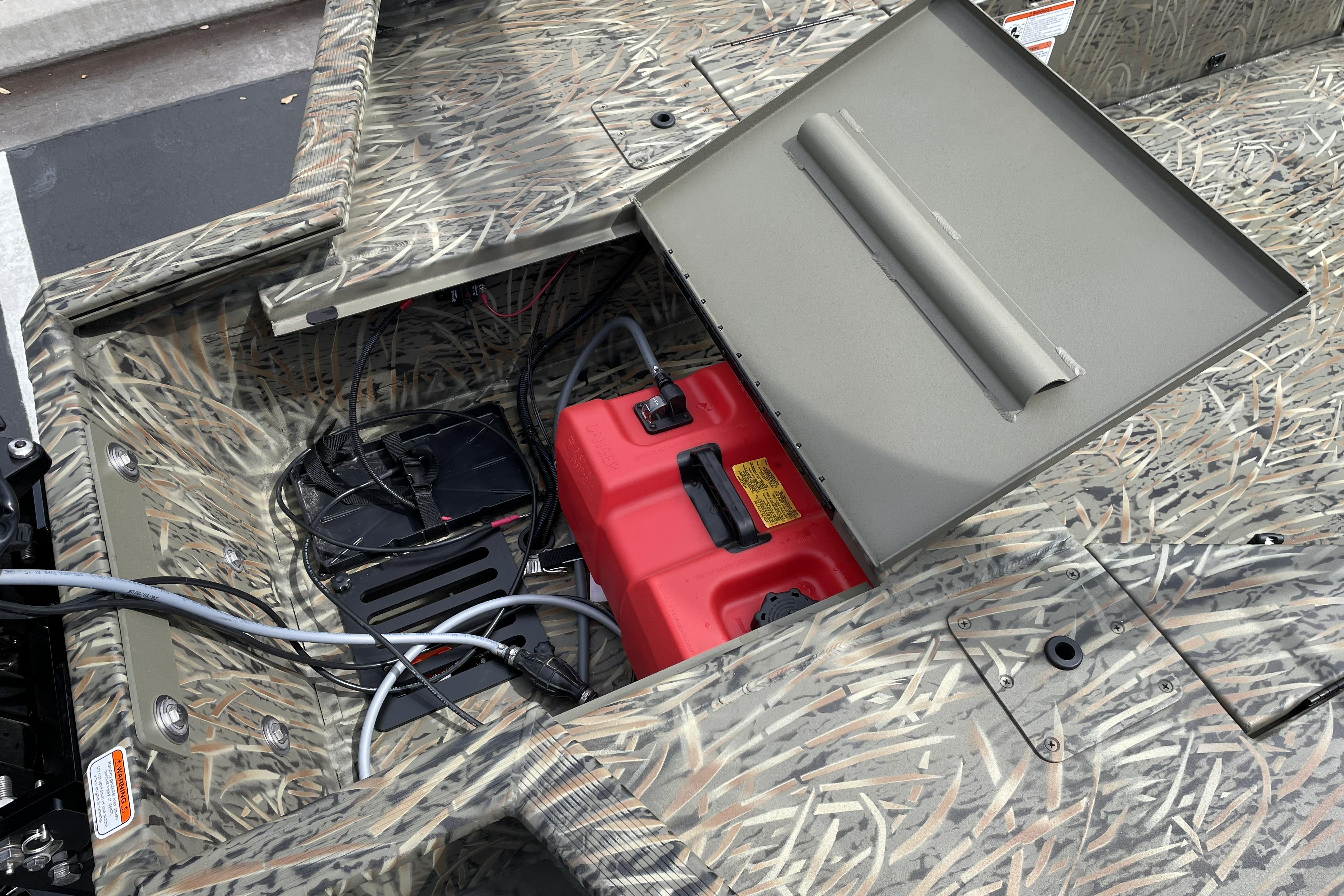 Open storage compartment in 2026 Tracker Grizzly 1756 T Marsh boat, revealing wiring and red fuel tank.