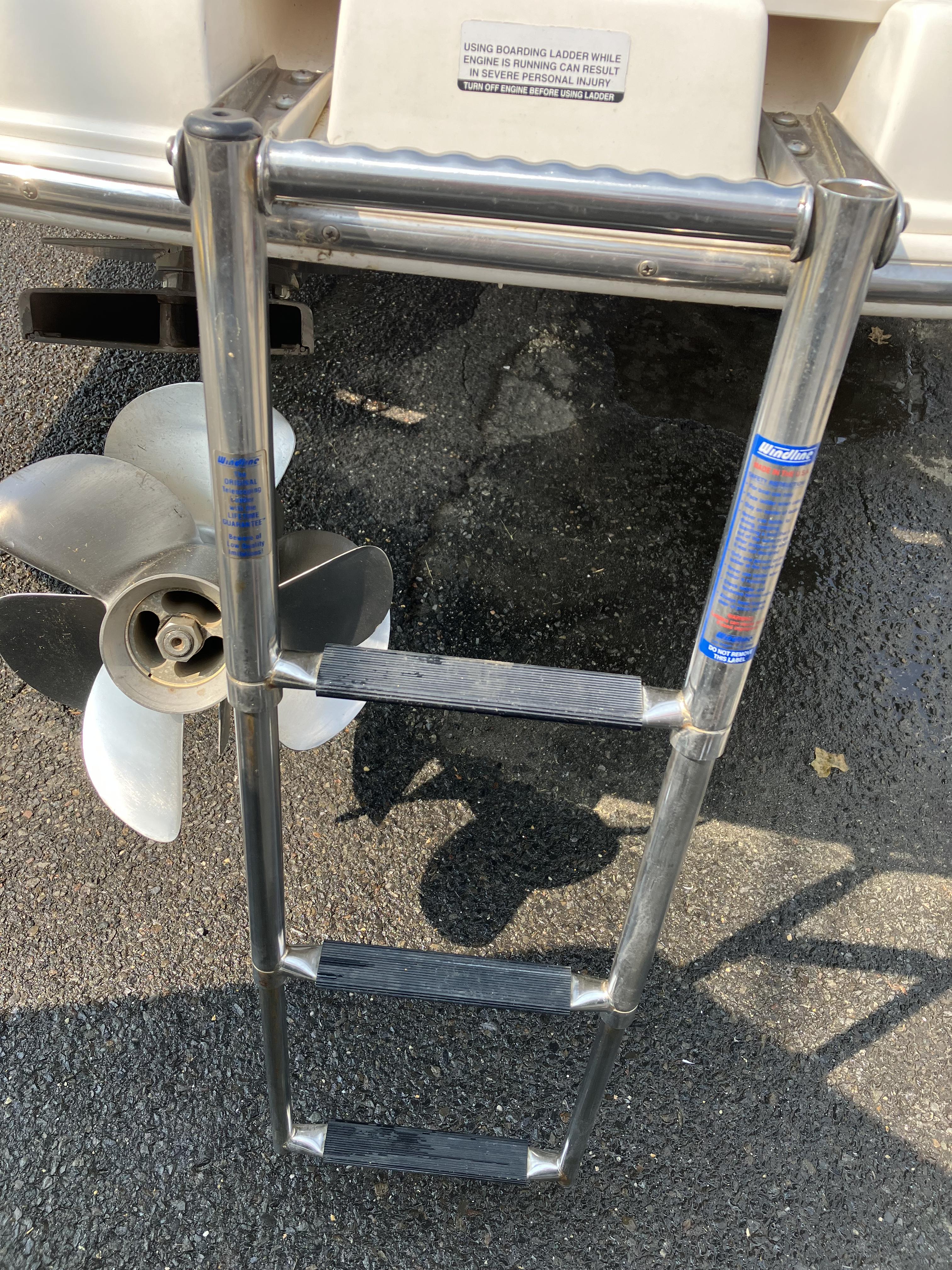 A metal swim ladder is attached to the back of a boat, next to a propeller.