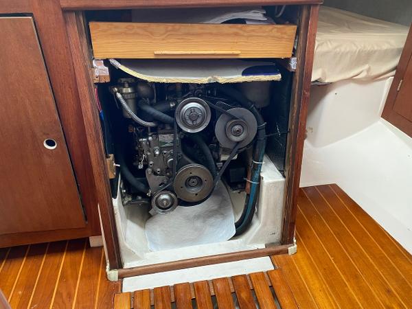 Engine compartment of a 1984 Hunter 31 sailboat, featuring visible belts and wooden cabinetry.