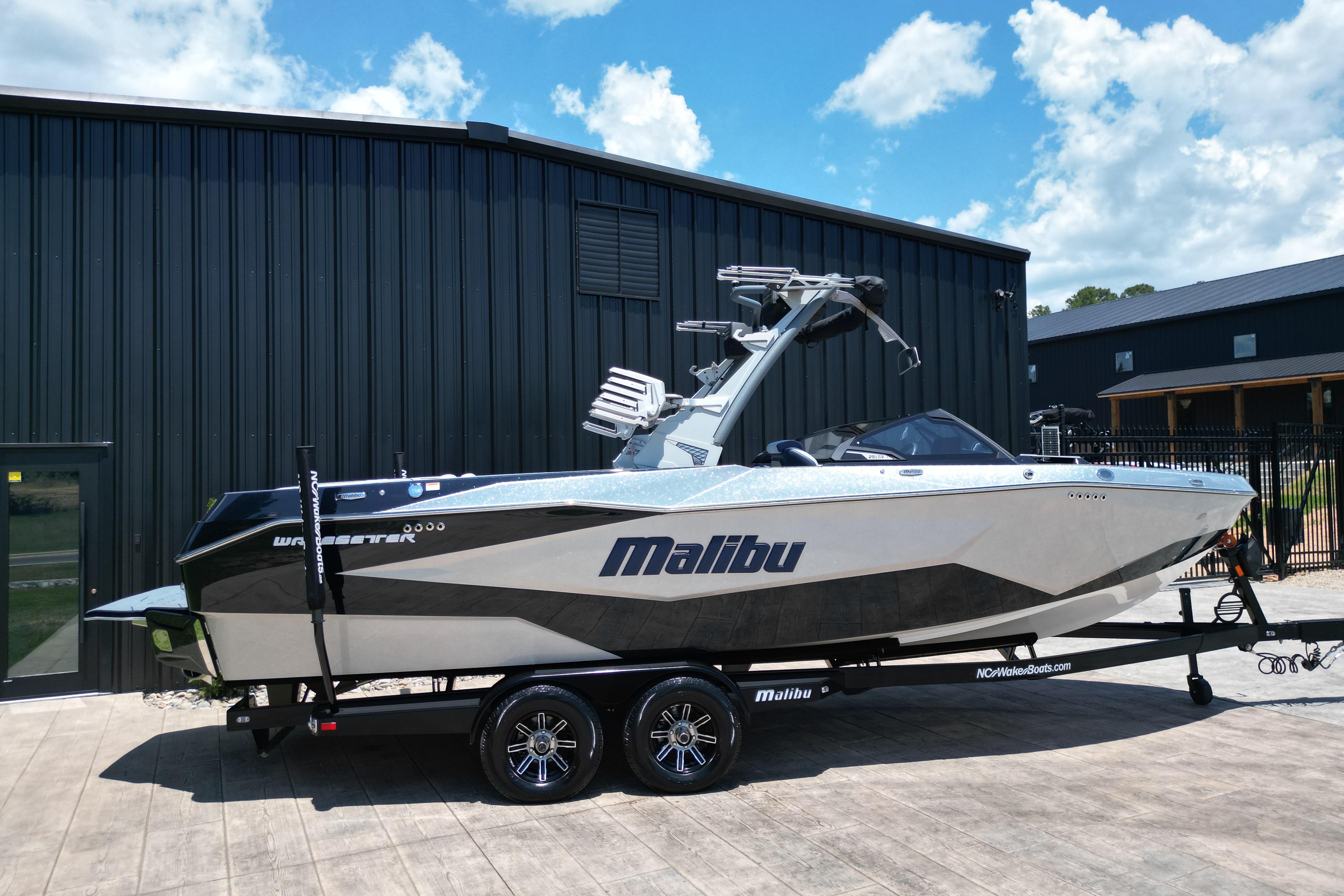 2025 Malibu Wakesetter 25 LSV boat on trailer, parked outside black building.