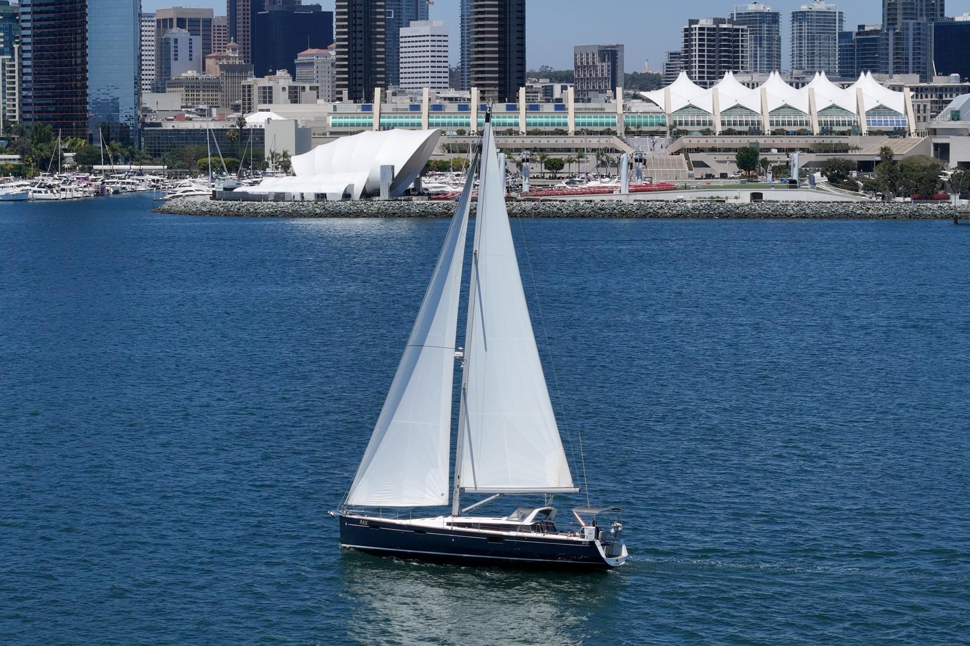 Sailing yacht Beneteau Sense 50, 2017 model, cruising near urban waterfront skyline.