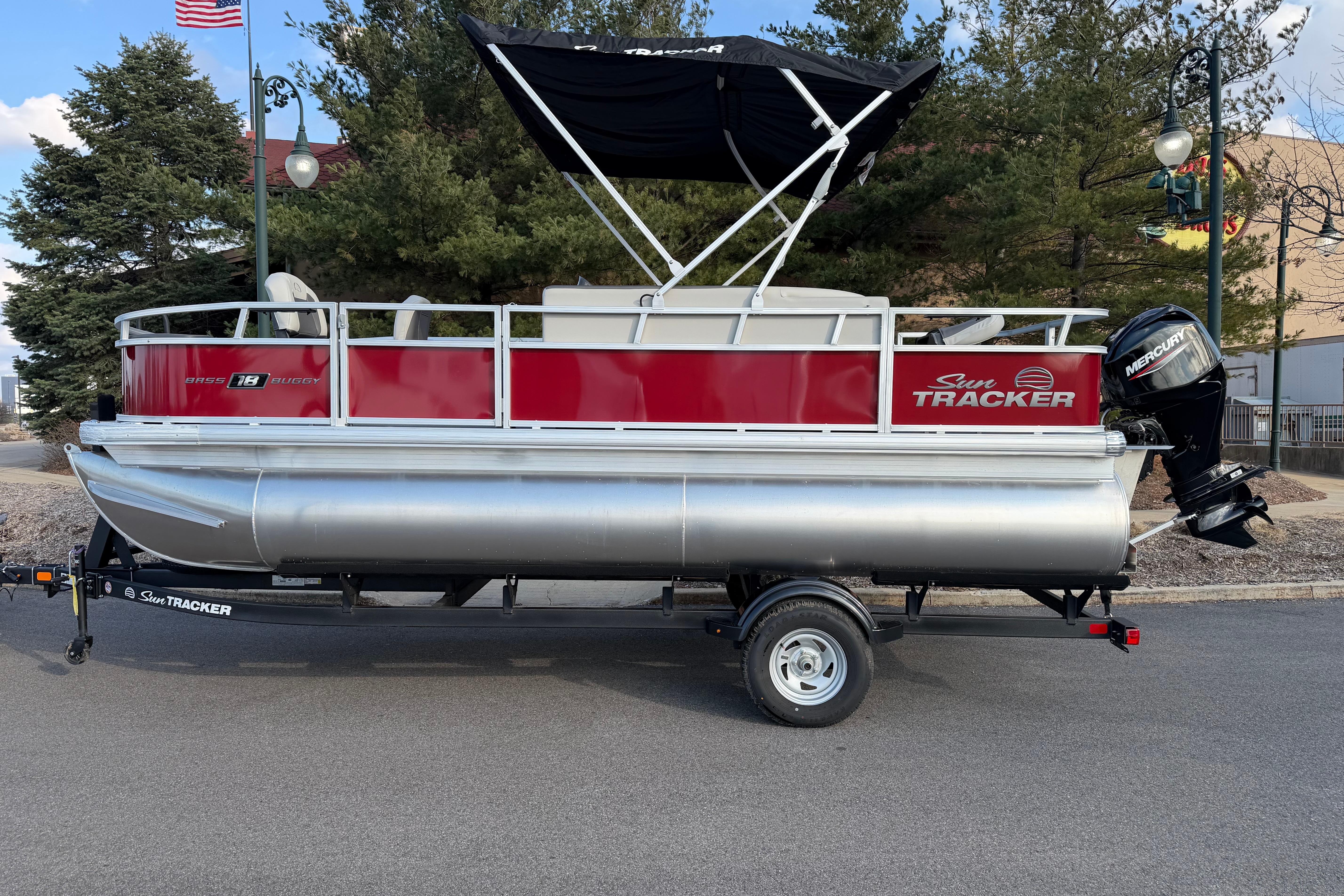 2026 Sun Tracker Bass Buggy 18 DLX pontoon boat on trailer, parked outdoors.