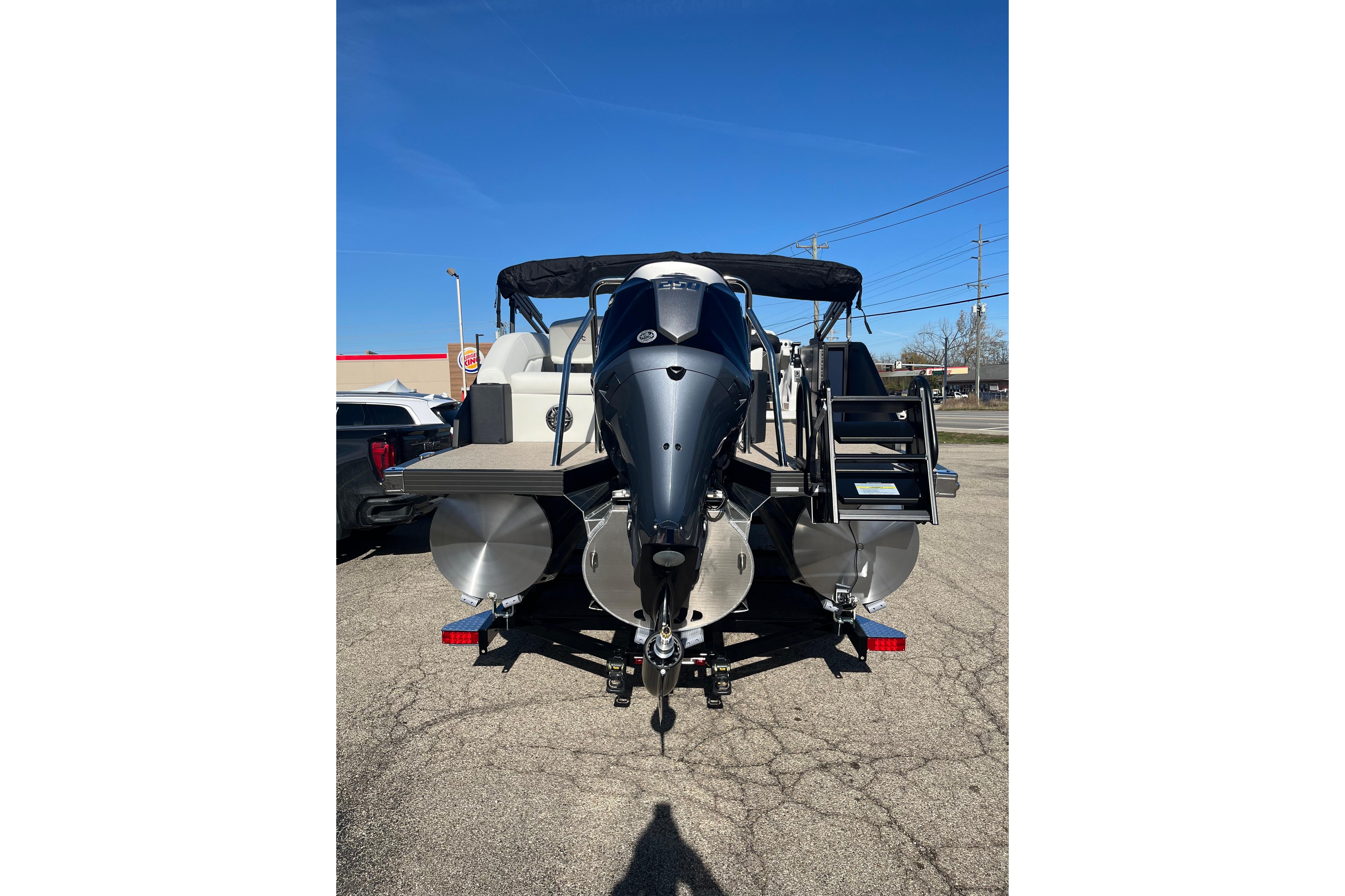 2026 Evotti 523CS pontoon boat with outboard motor, parked on pavement under clear blue sky.