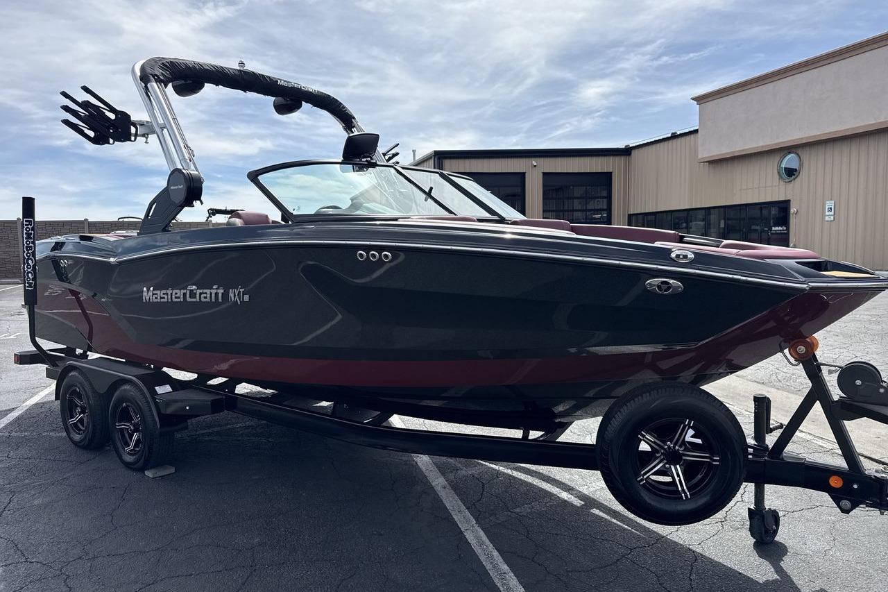 2023 MasterCraft NXT22 boat on trailer, parked outdoors under a cloudy sky.