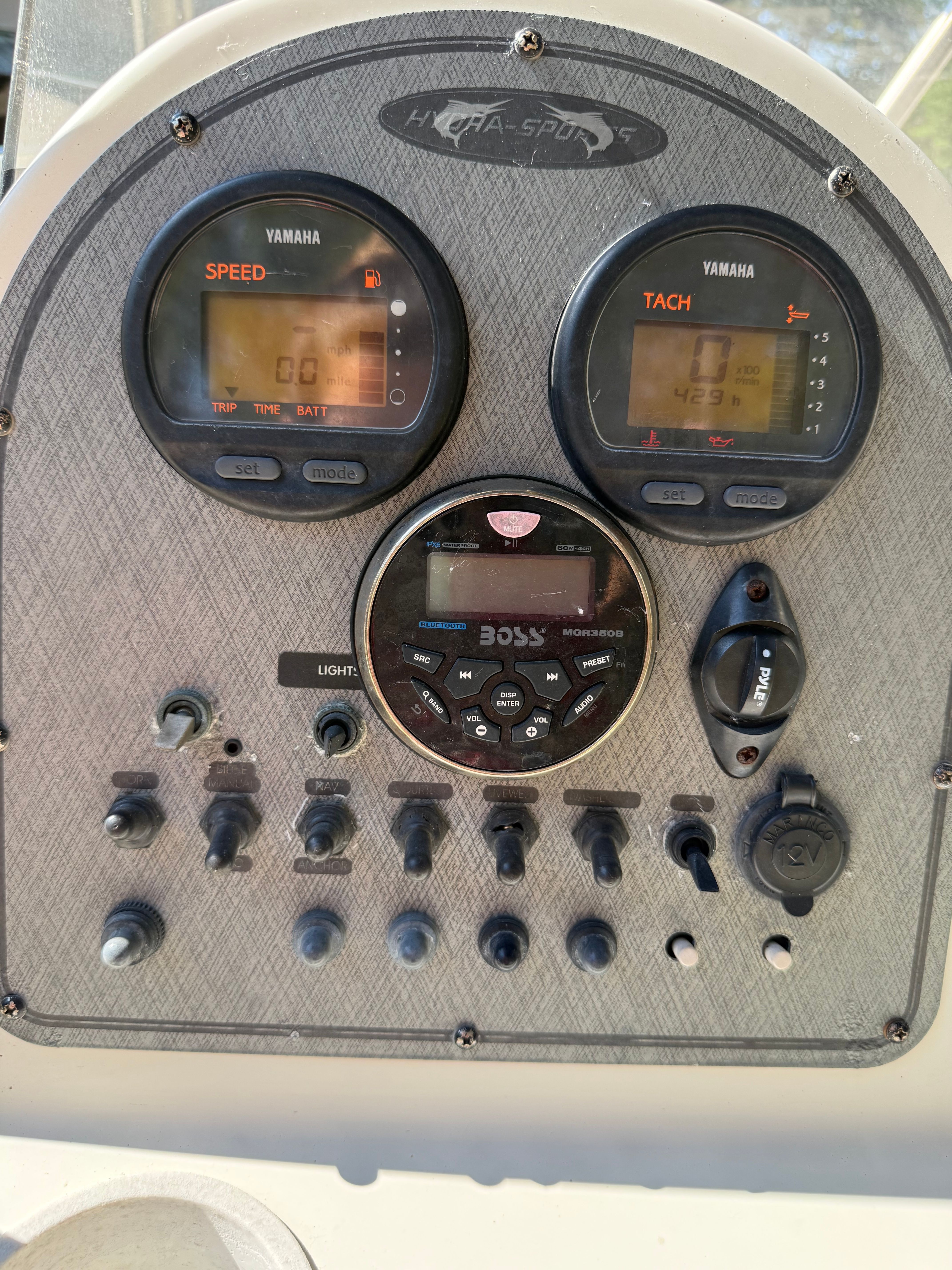 Boat dashboard with speed and tachometer displays, and various switches.