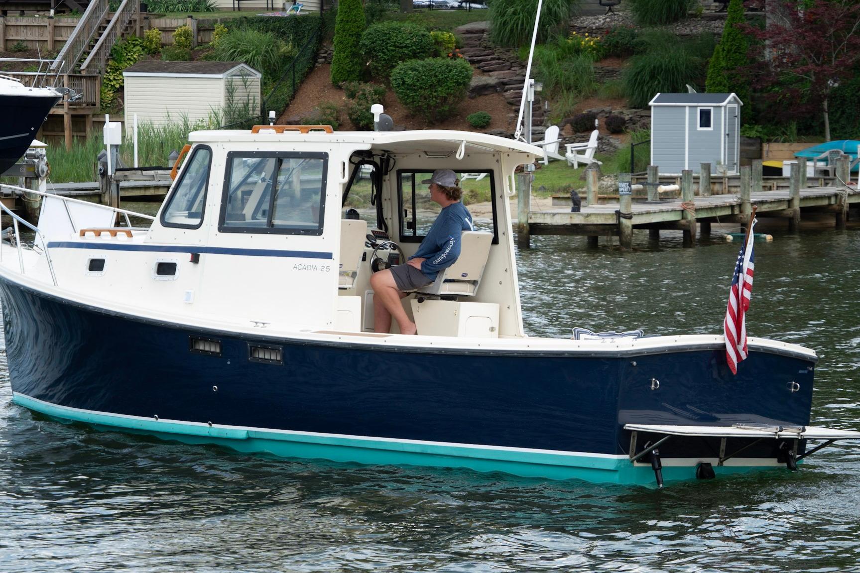 2006 Atlas Boat Works Acadia 25 cruising on a scenic waterfront with dock and greenery.