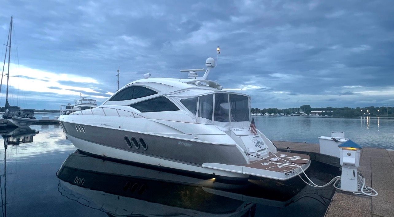 A luxury motor yacht docked at a calm pier under a cloudy sky.