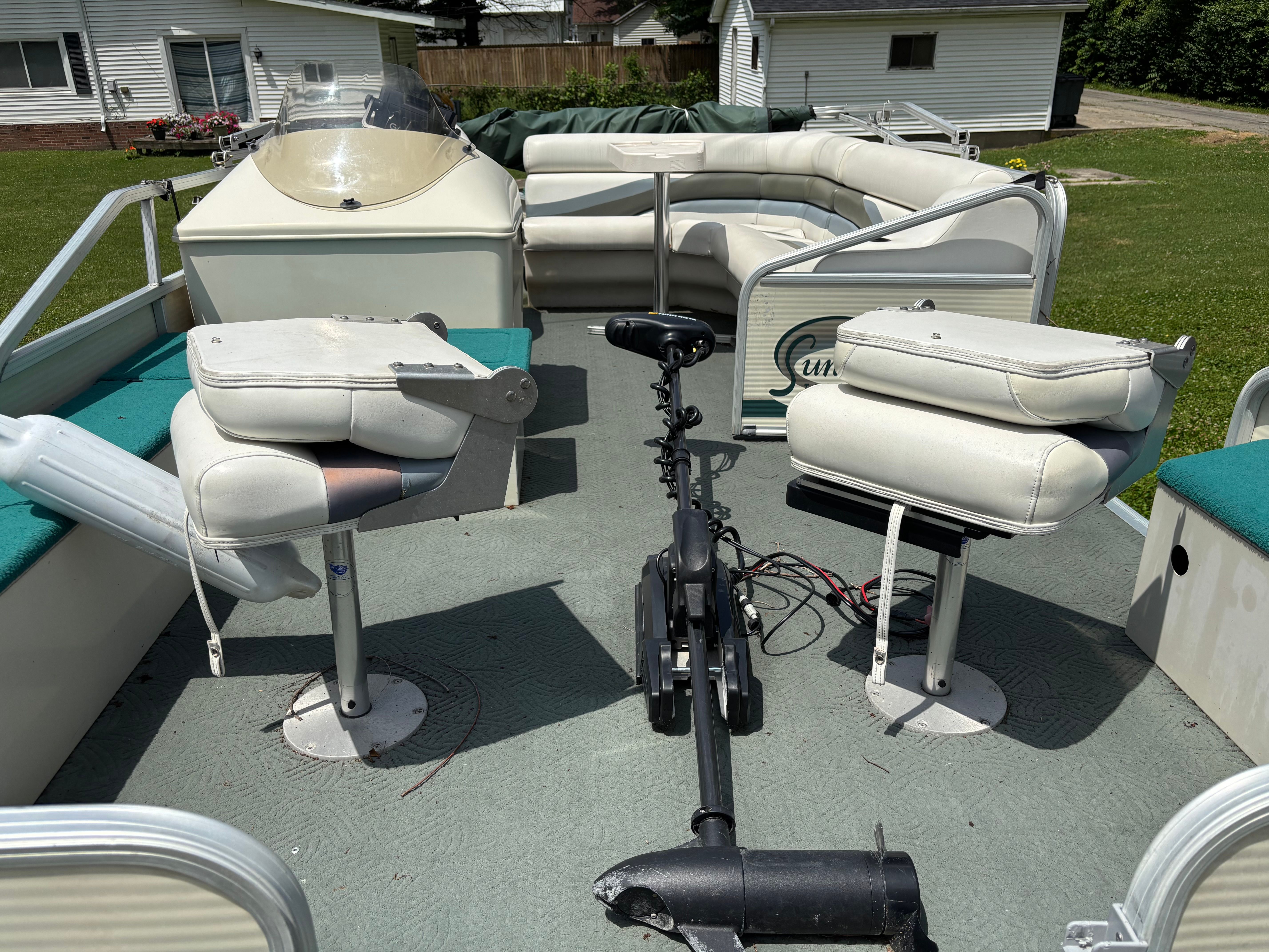The image shows a pontoon boat with white seats and a helm. It is on a lawn.