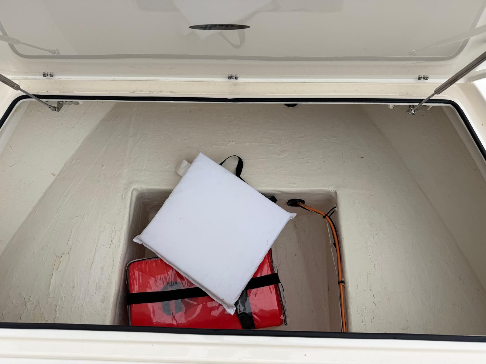 An open storage compartment with red and white cushions and a cable inside.