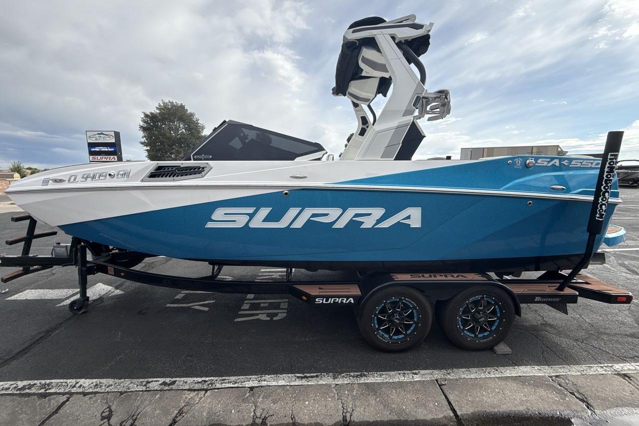 2024 Supra SA 550 boat on trailer, blue and white design, parked outdoors.