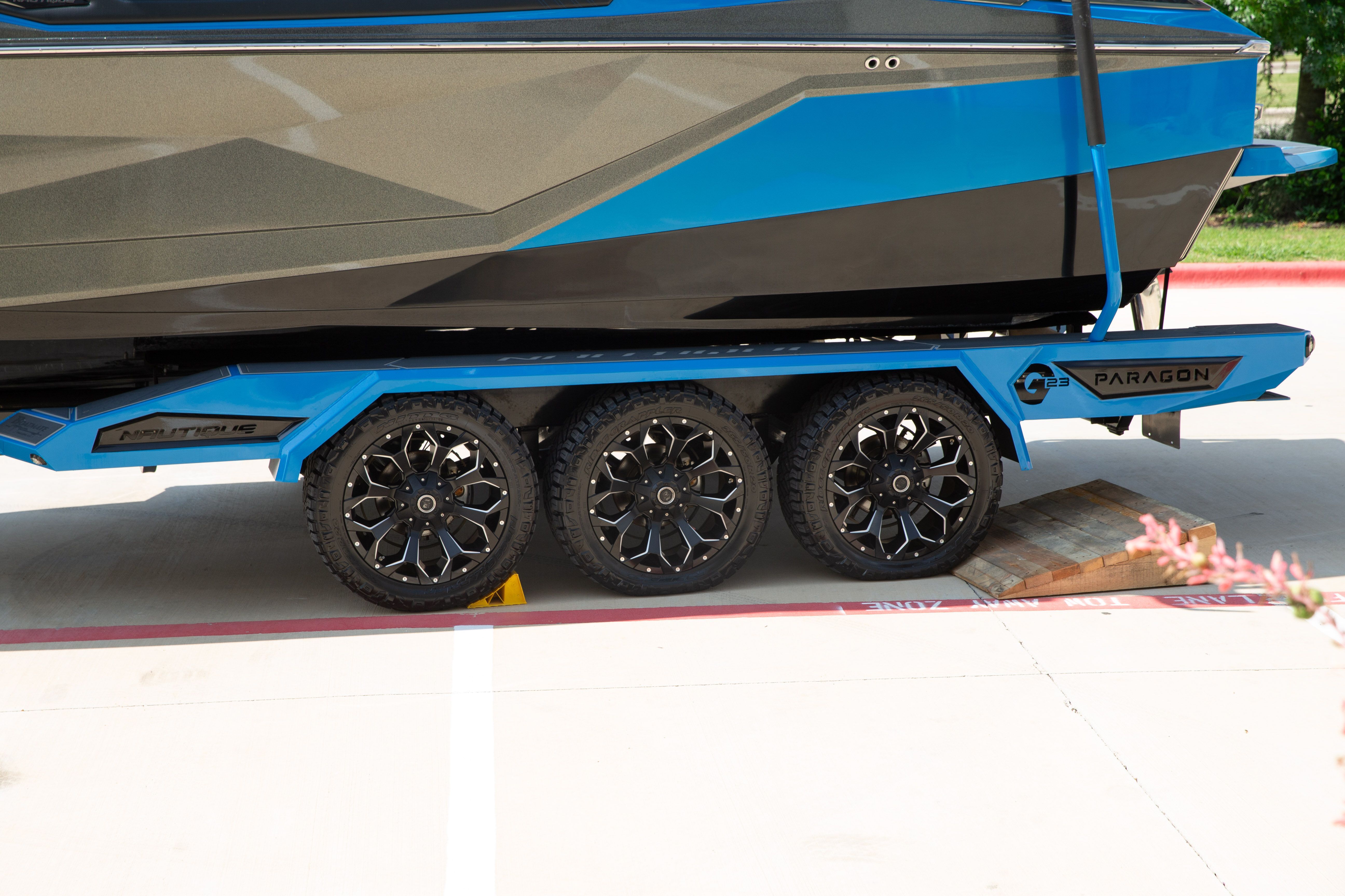 A blue and black boat on a trailer with three axles and stylish wheels.