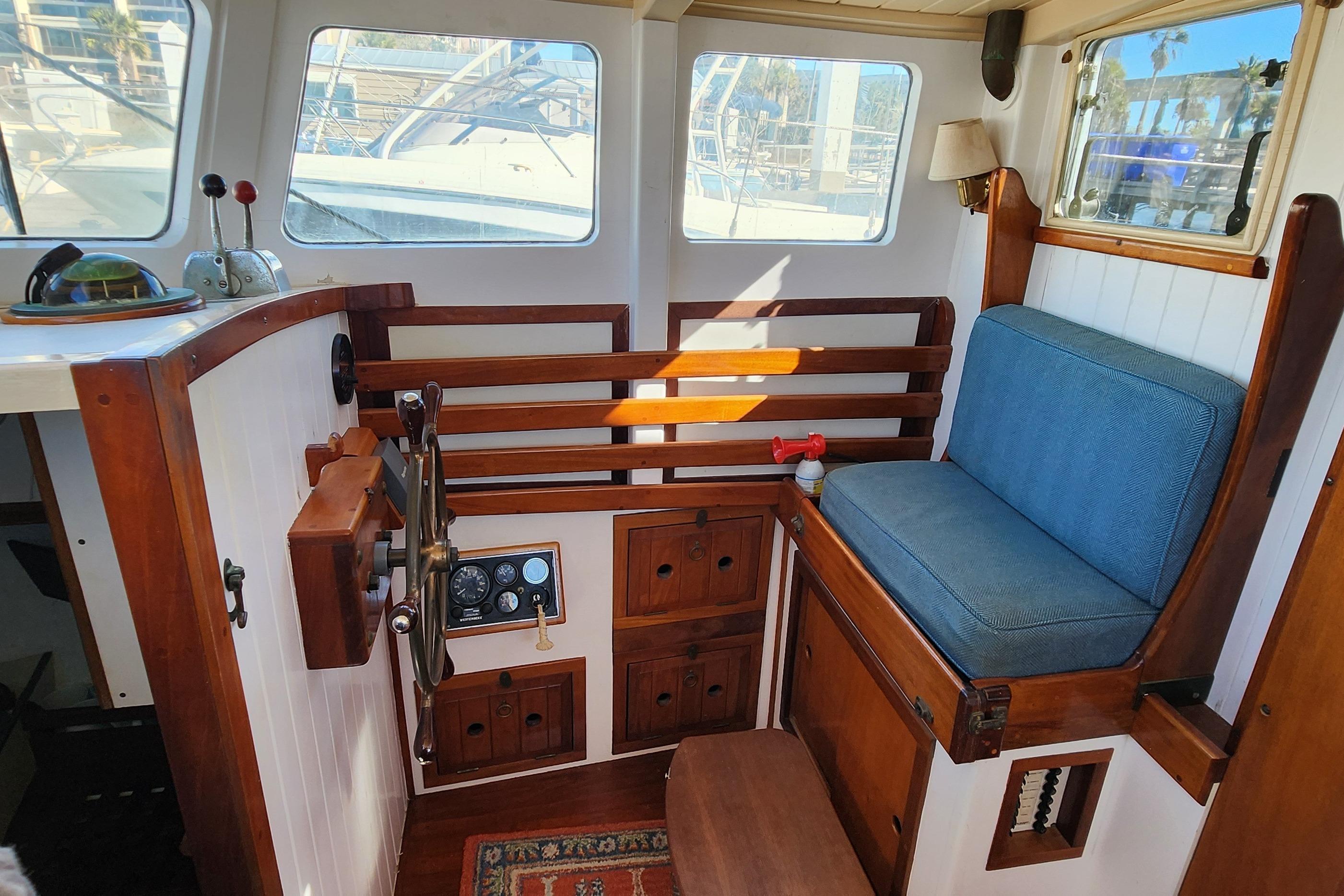 Cozy interior of 1996 Tillotson-Pearson Motorsailer 32 with wooden helm and blue cushioned seat.
