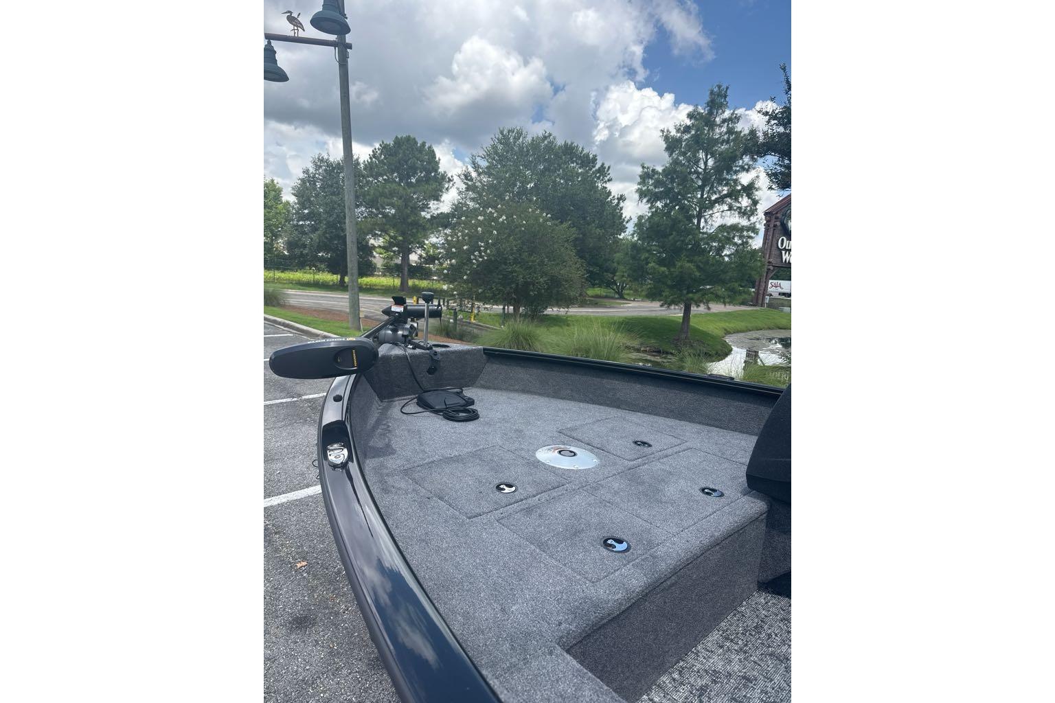 2026 Tracker Pro Guide V-16 SC boat with trolling motor, parked near trees and pond.
