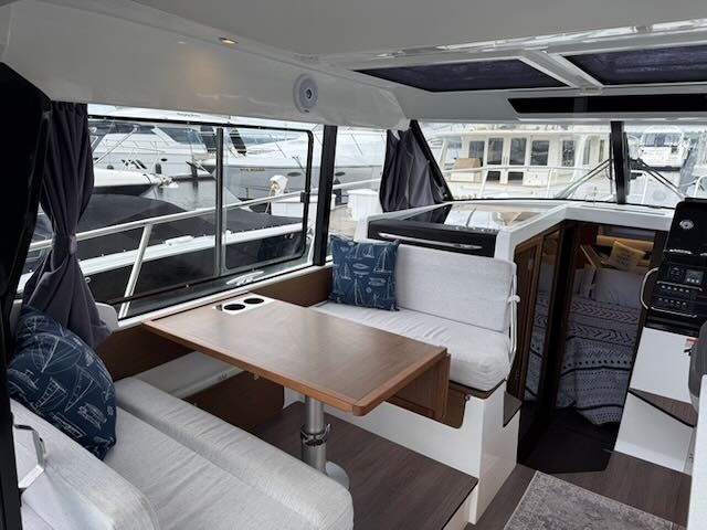 Interior of Jeanneau NC 1095 with table, benches, and windows overlooking the marina.