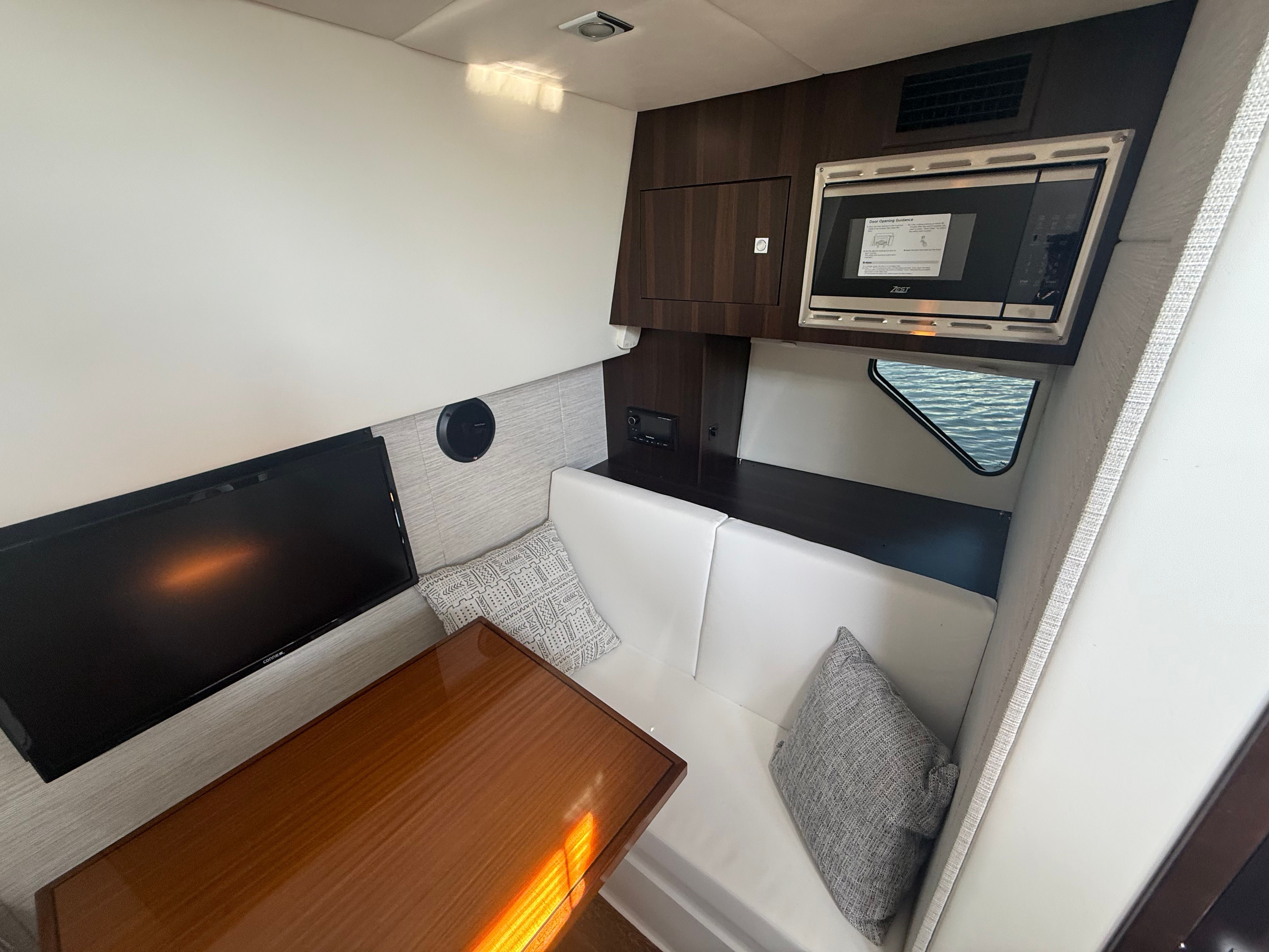 Interior of a modern yacht featuring a sleek wooden table, white seating, and a built-in microwave.