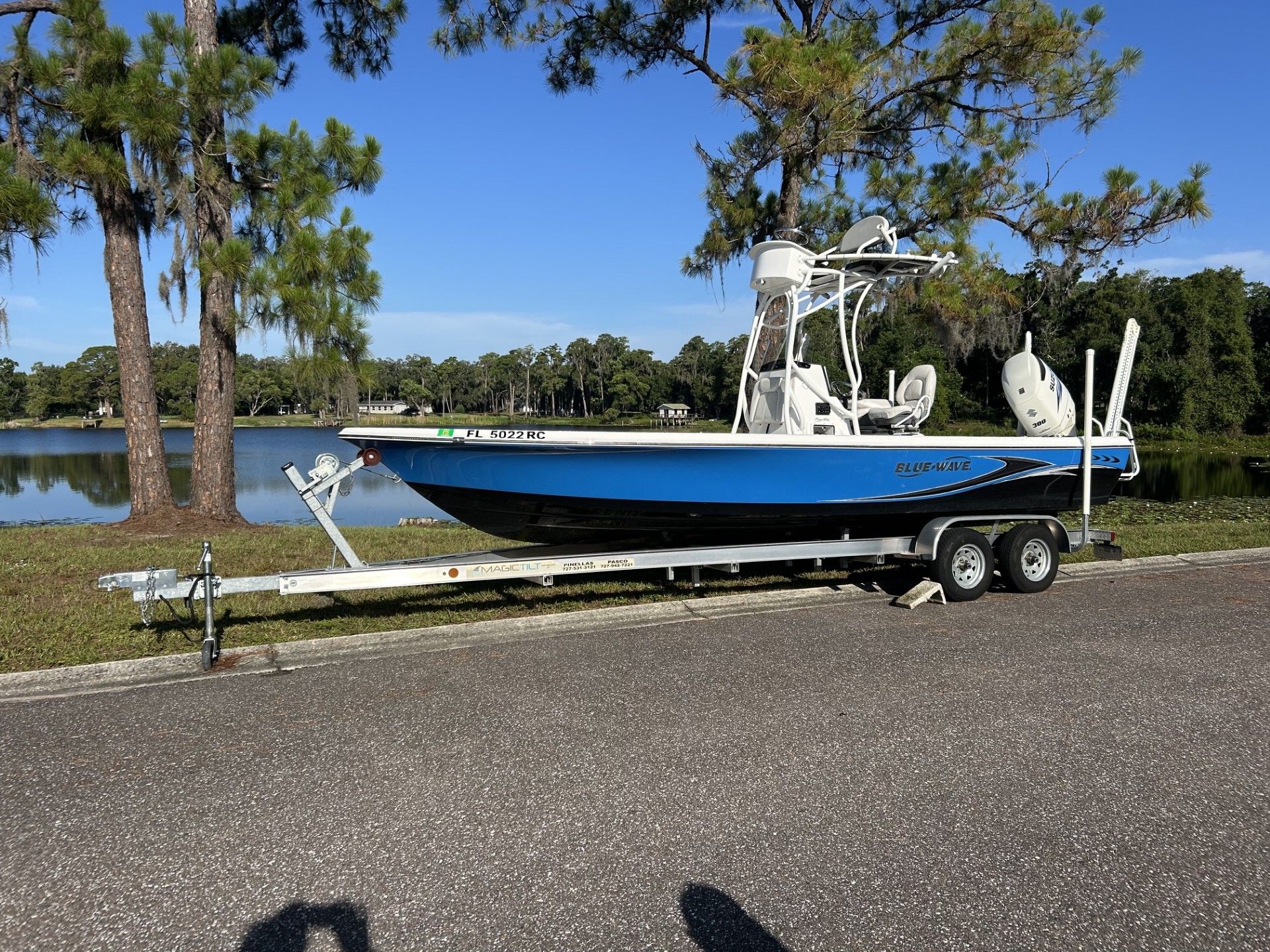 A 2016 Blue Wave 2400 PureBay boat on a trailer, parked beside a tranquil lake.