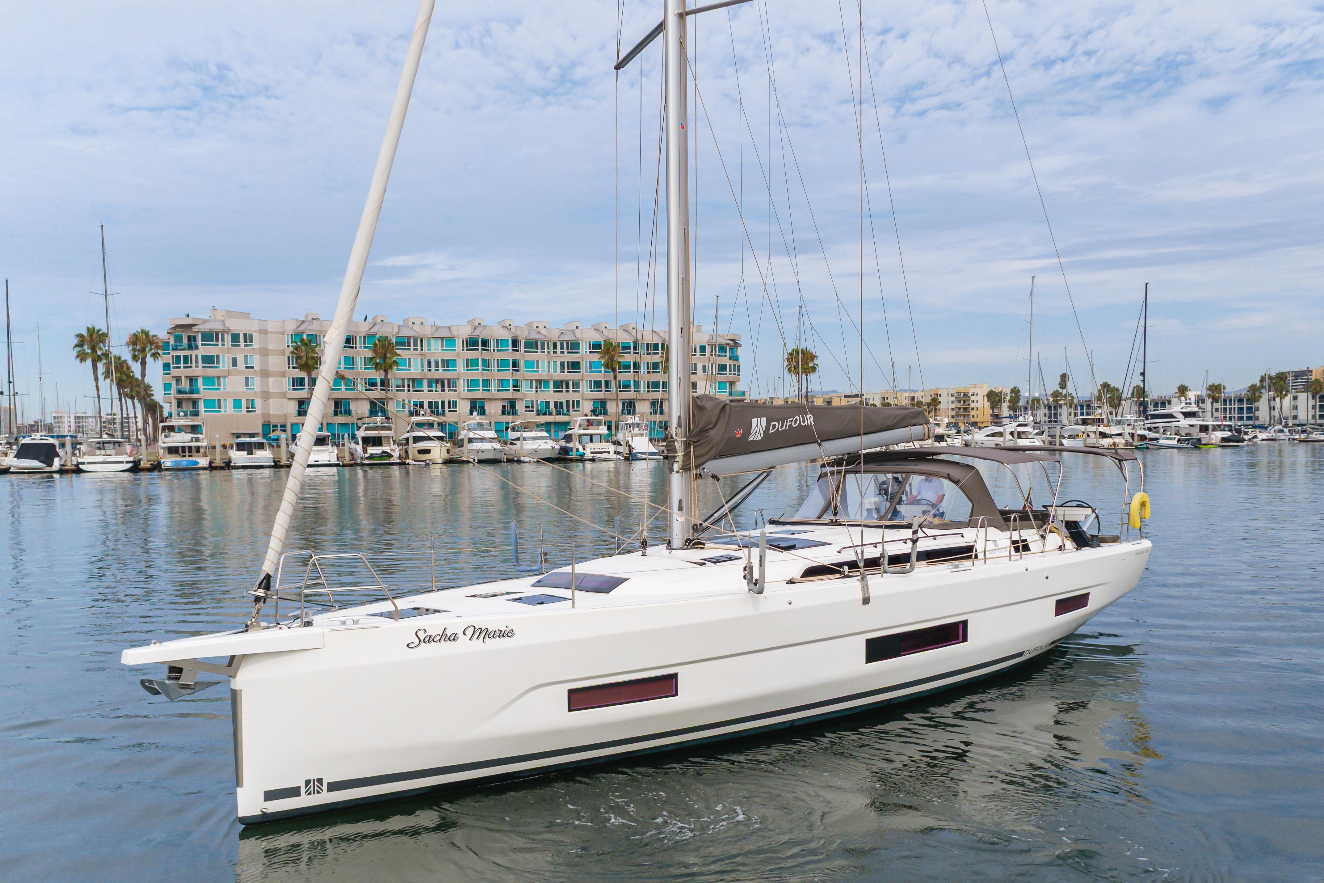 2024 Dufour 470 sailboat docked in marina, modern design, calm waters, coastal buildings.